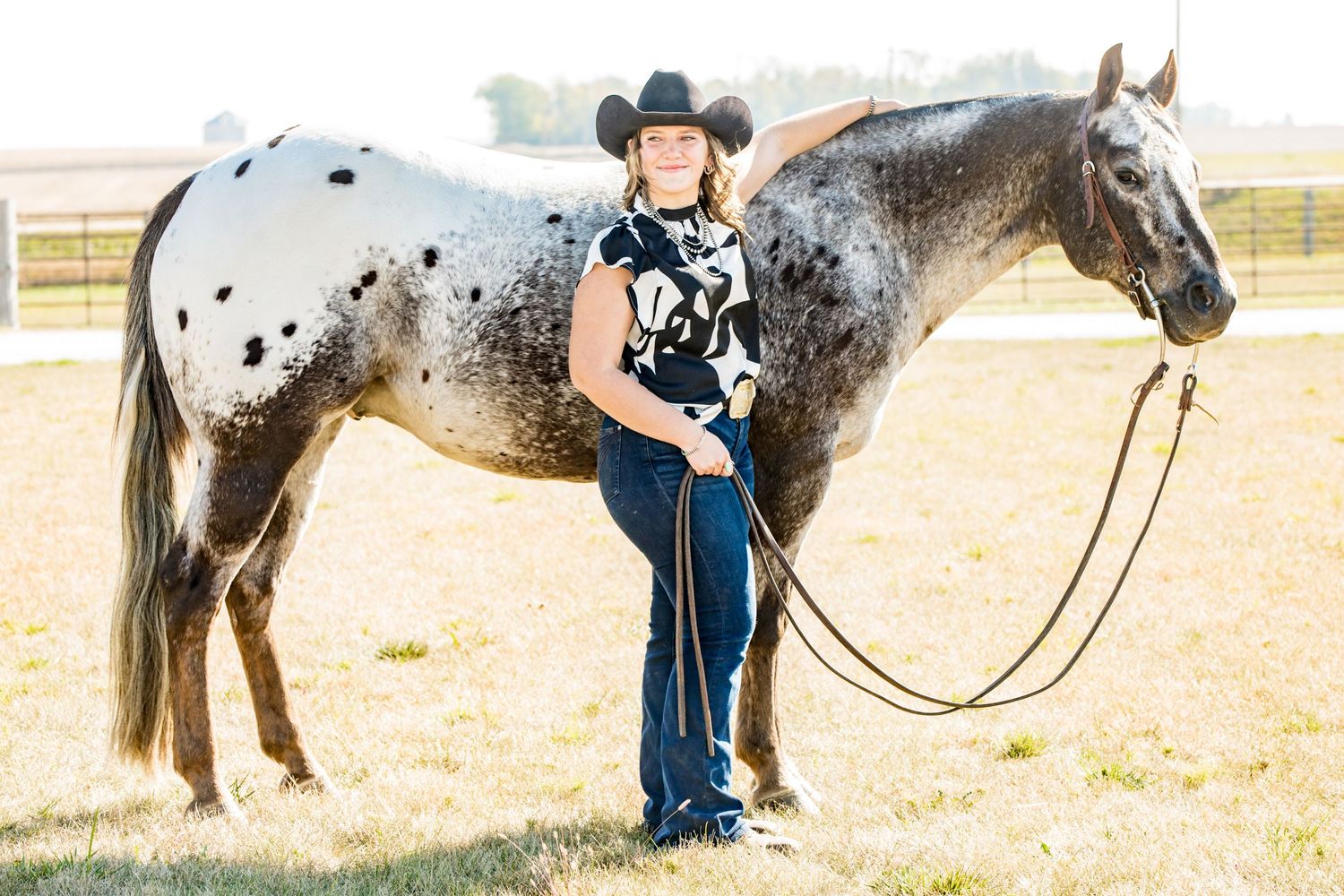 An appaloosa horse with black and white spotted coat stands with someone in western attire.