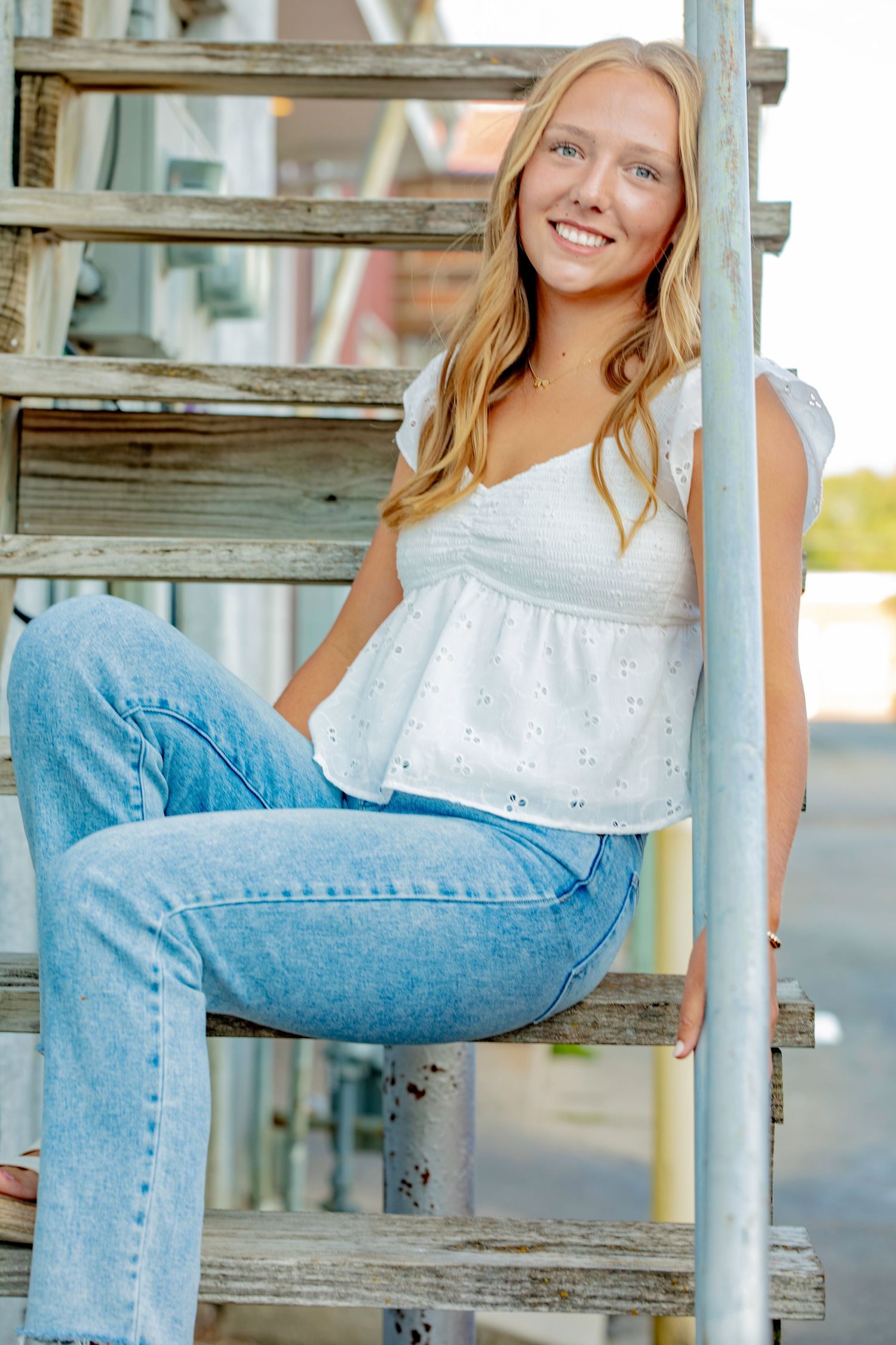 Person in jeans relaxing on rustic wooden steps outdoors during golden hour sunlight.