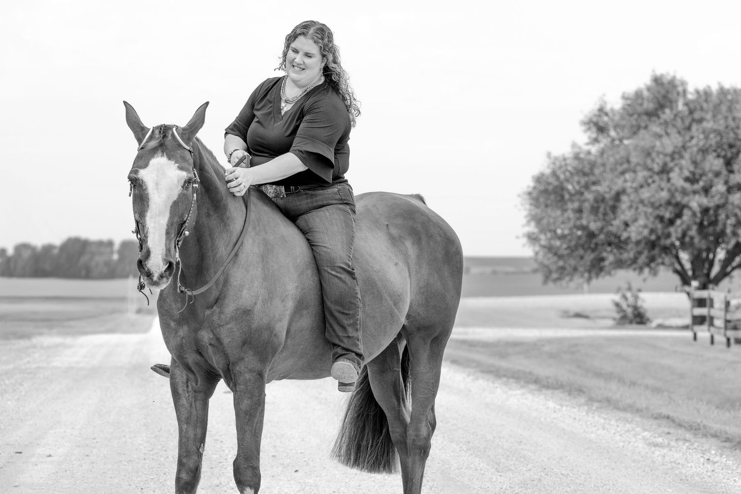 Woman smiling while sitting bareback on a chestnut horse on a rural road, black and white photo.