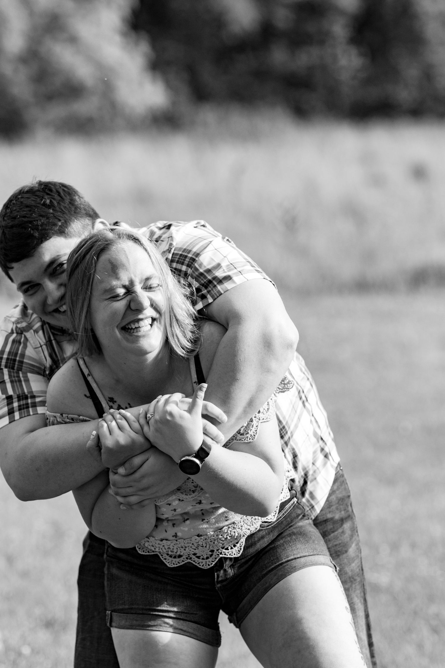 A playful couple sharing a joyful moment together in a sunlit field.