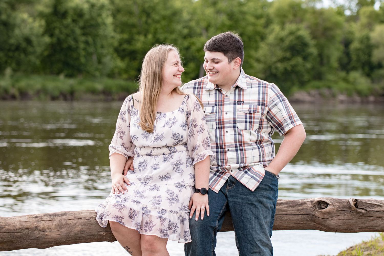 A couple sitting together on a log by a river sharing a tender moment.