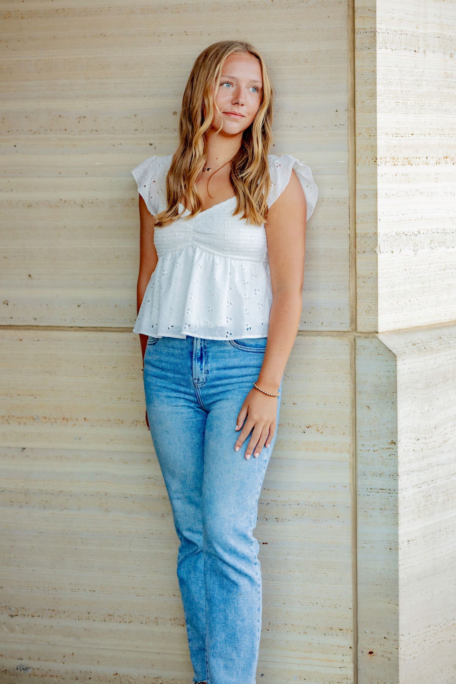 Person wearing white eyelet crop top and light blue mom jeans poses against beige textured wall.