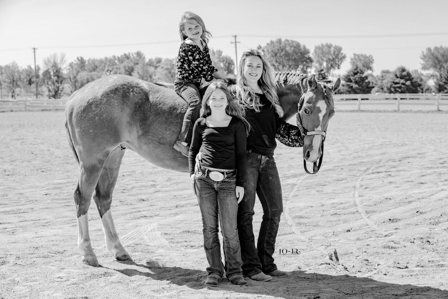 A black and white photo shows a small horse or pony in a rural field with three people standing beside it.