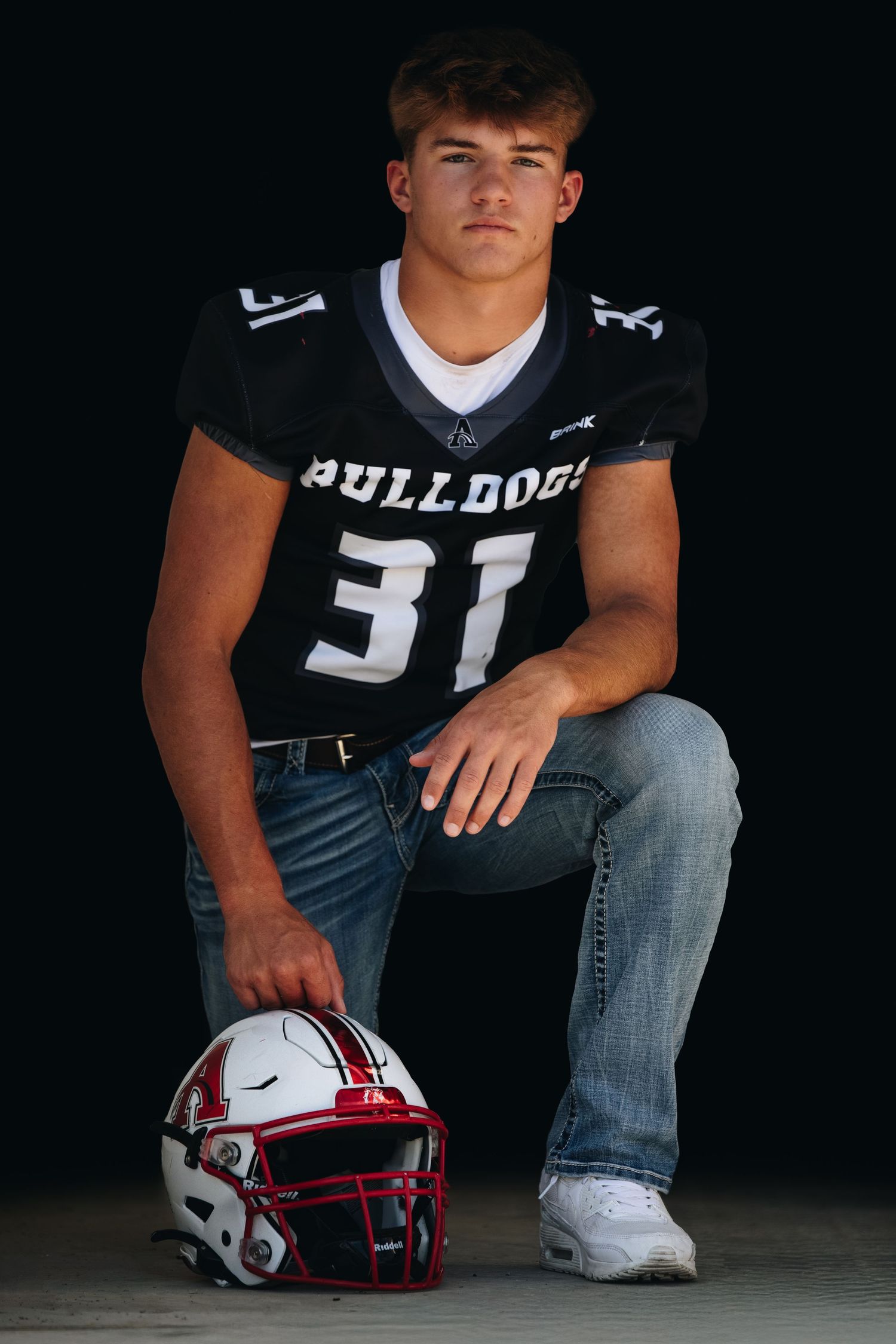 Football player in number 31 Bulldogs jersey kneels with helmet on ground.