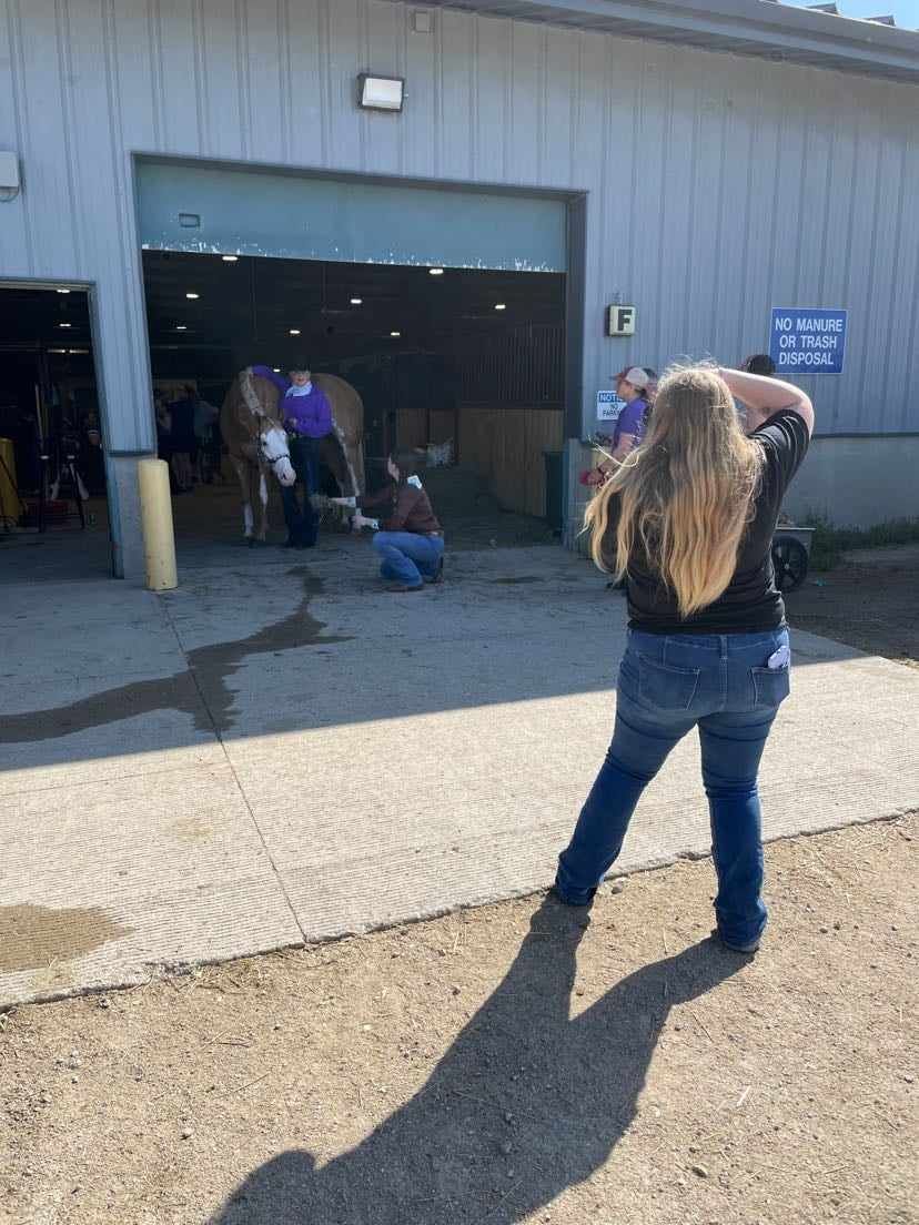 Person taking a photo outside a building entrance as people gather near an open garage-style door in daylight.