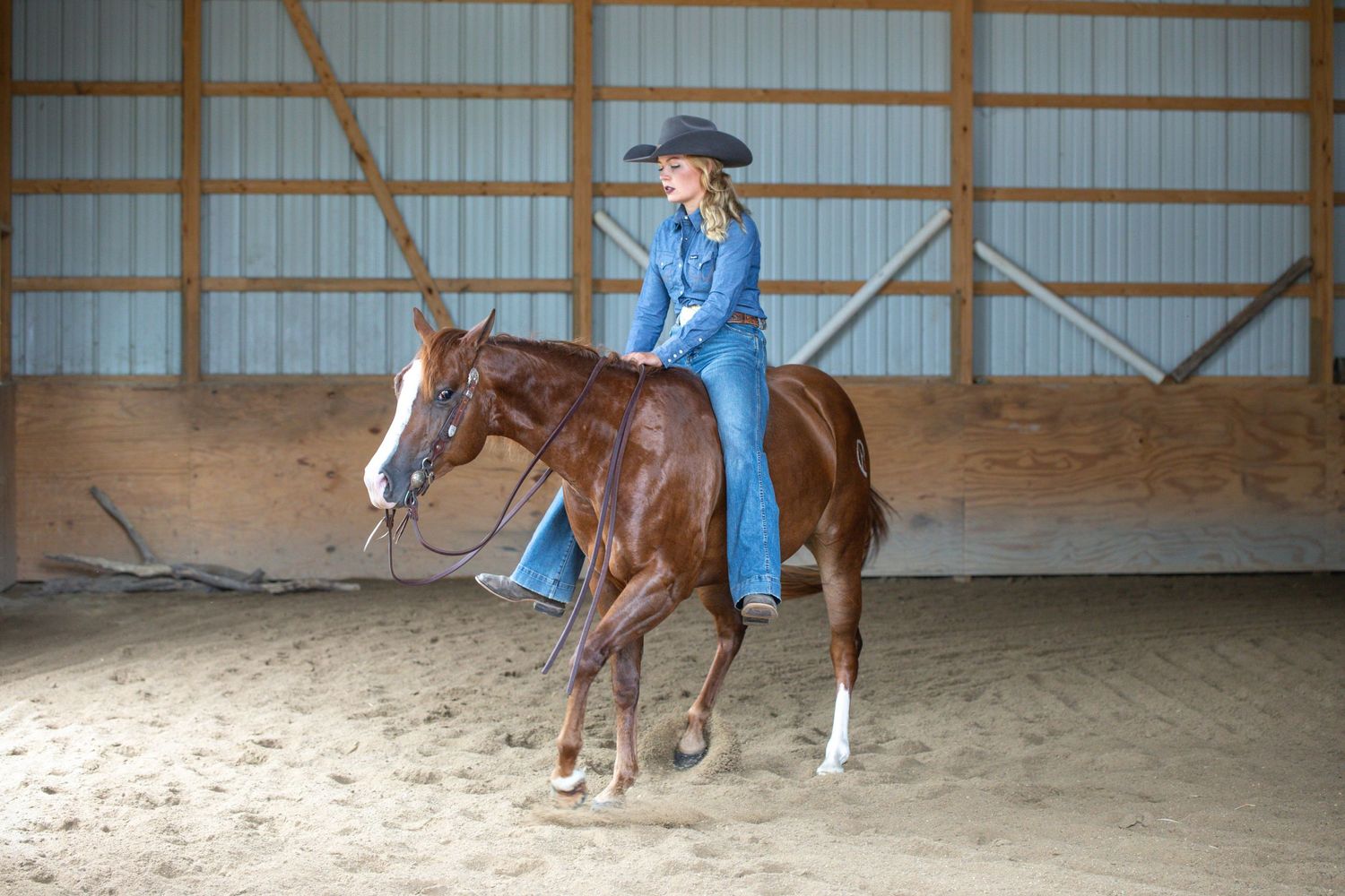 A horse and rider practice in an indoor arena with wooden beams visible.