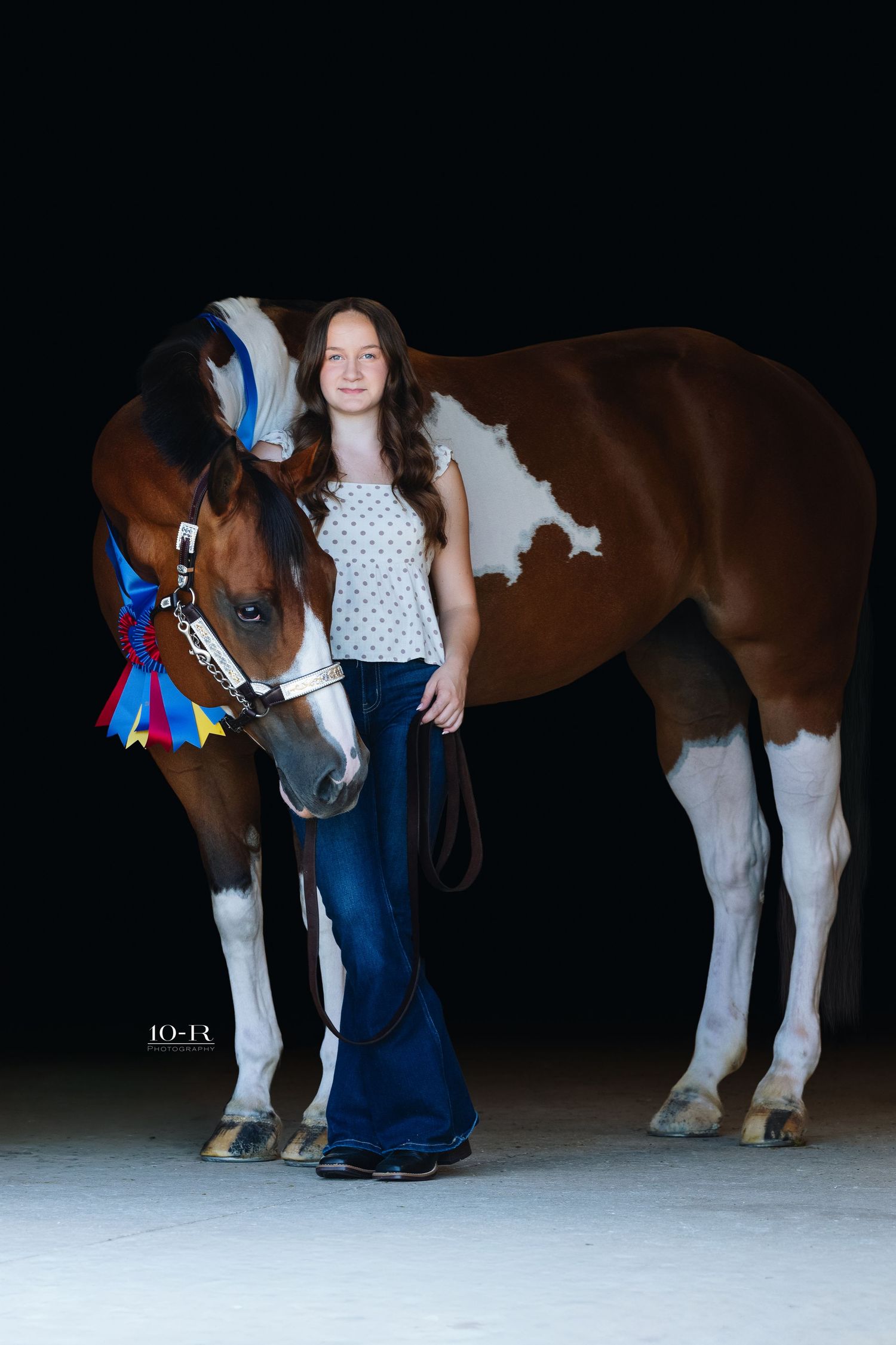 Young girl stands proudly beside her award-winning brown and white Paint horse adorned with colorful ribbons.