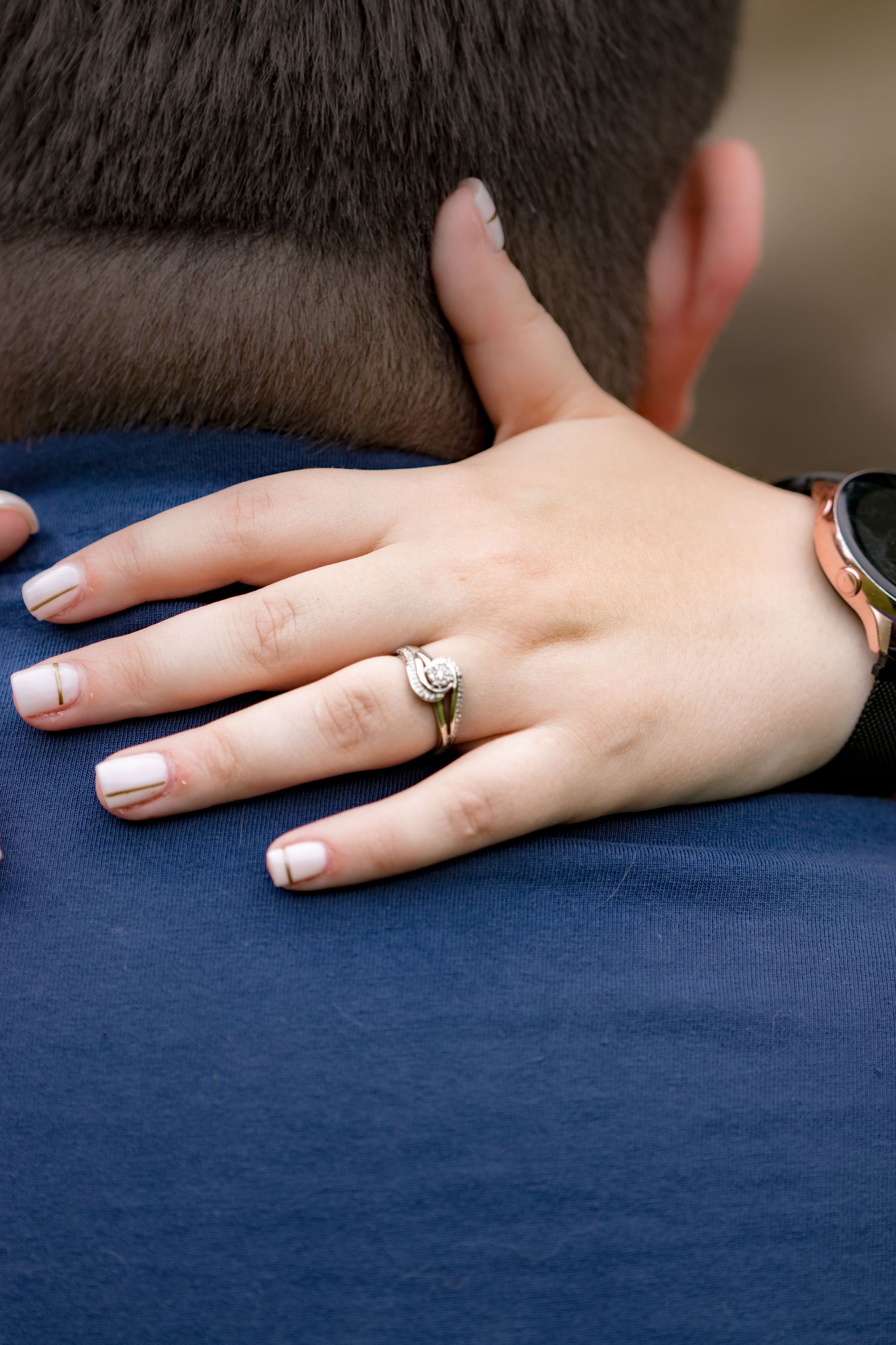A close up of an engagement ring on a hand resting on blue fabric.