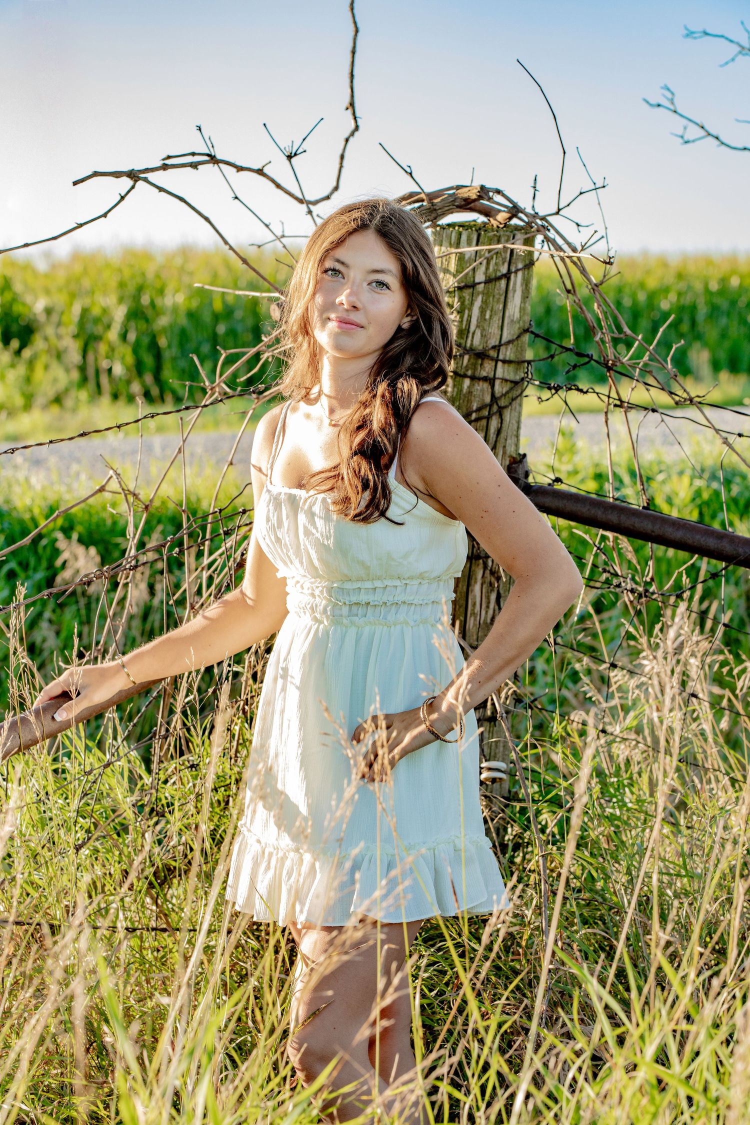 A white summer dress flows in the breeze among tall grasses and branches.