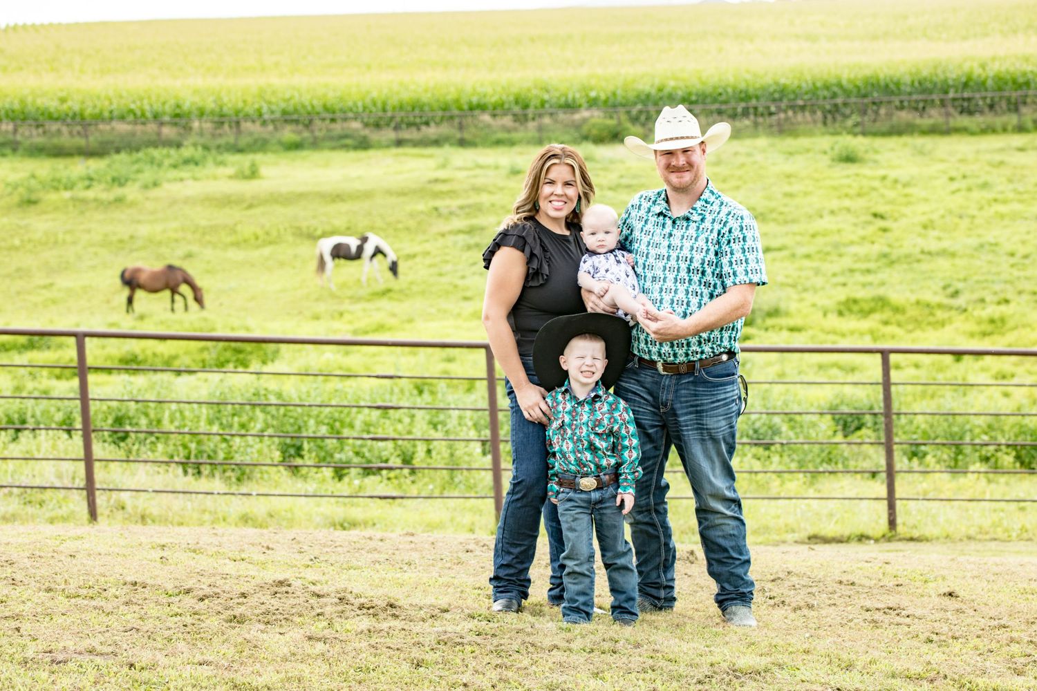 Family standing by fence overlooking pastoral horse pasture on sunny day.