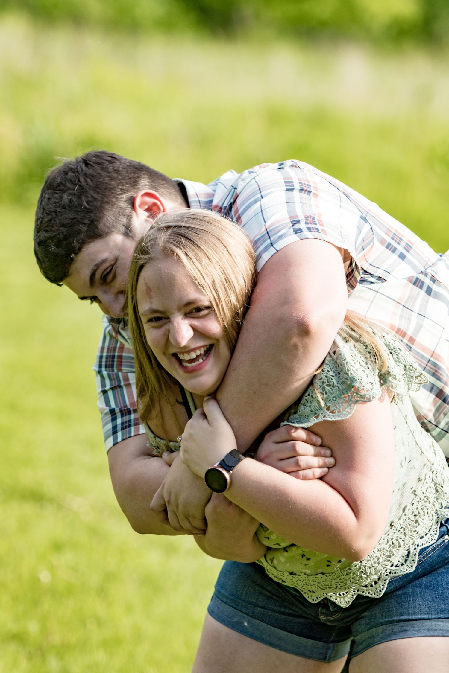 A couple laughs together while embracing in a sunny green field.