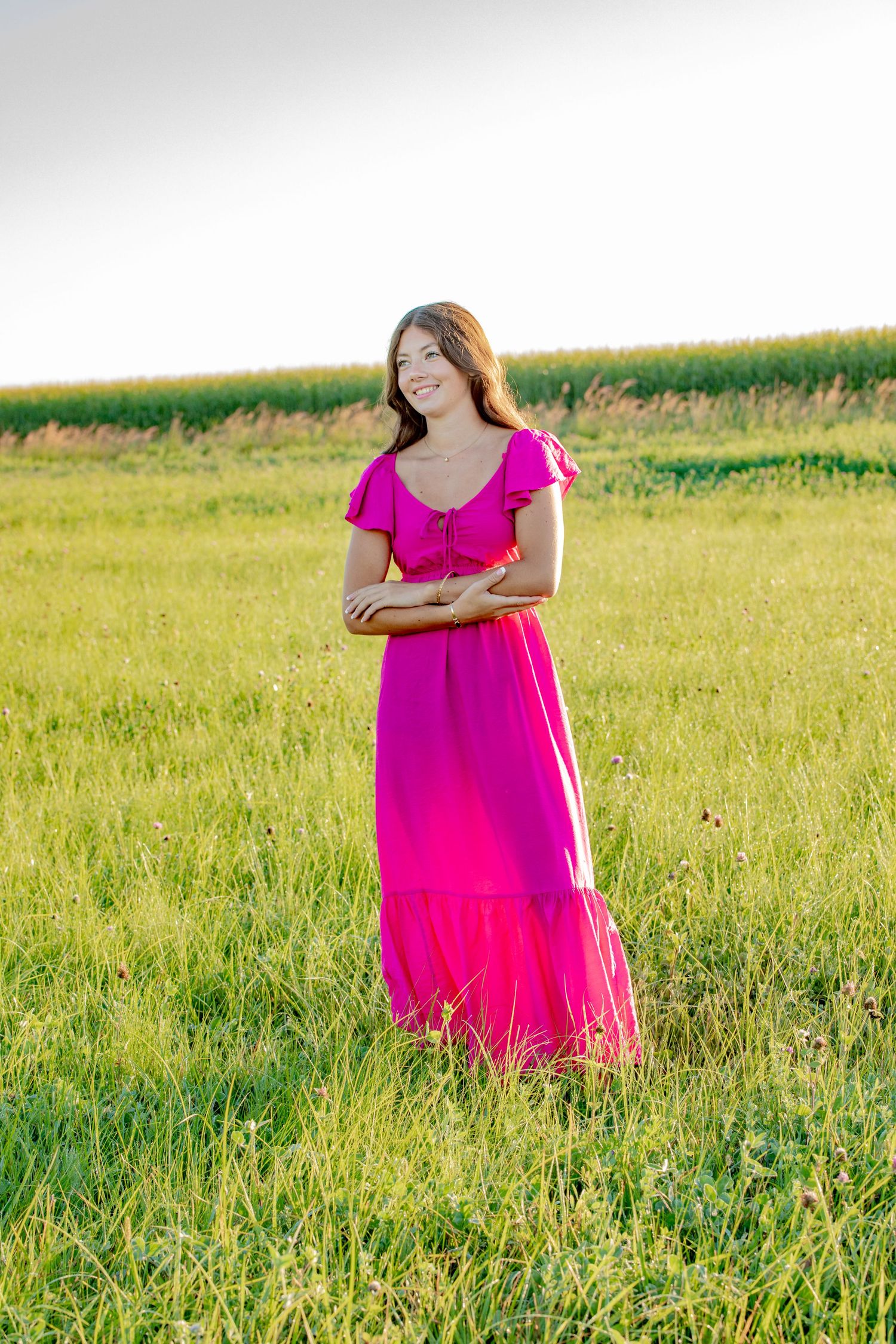 A bright pink dress creates a striking contrast against a lush summer meadow on a sunny afternoon.
