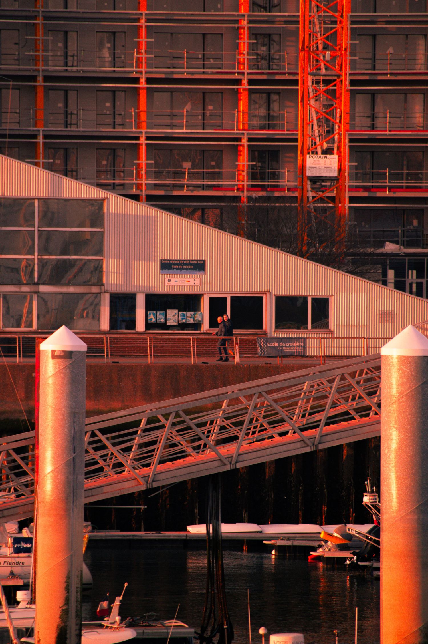 A marina dock with red-lit poles and metal framework reflects on calm water at sunset.