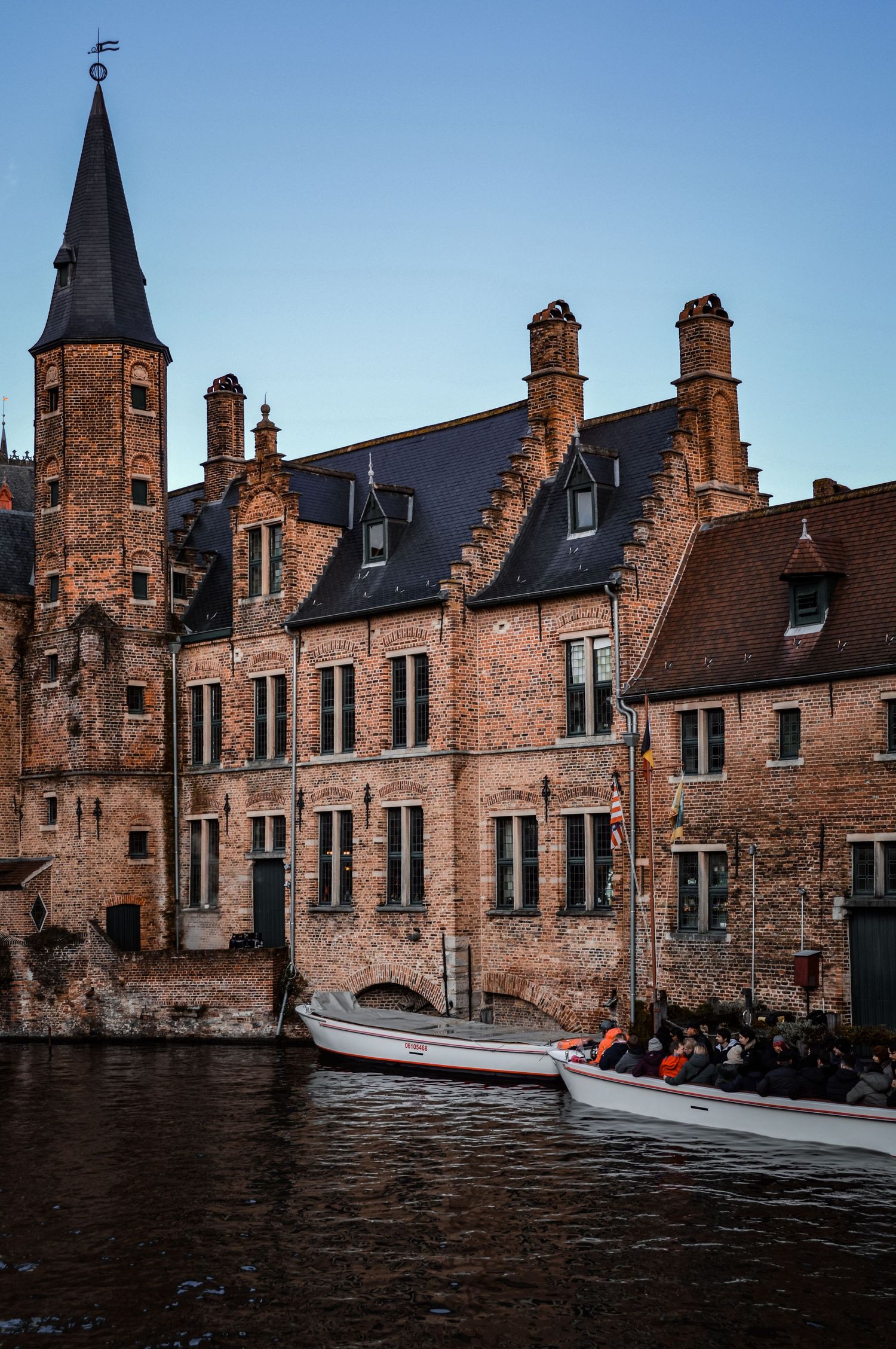 Medieval brick buildings along a canal with tourists in boat passing by.