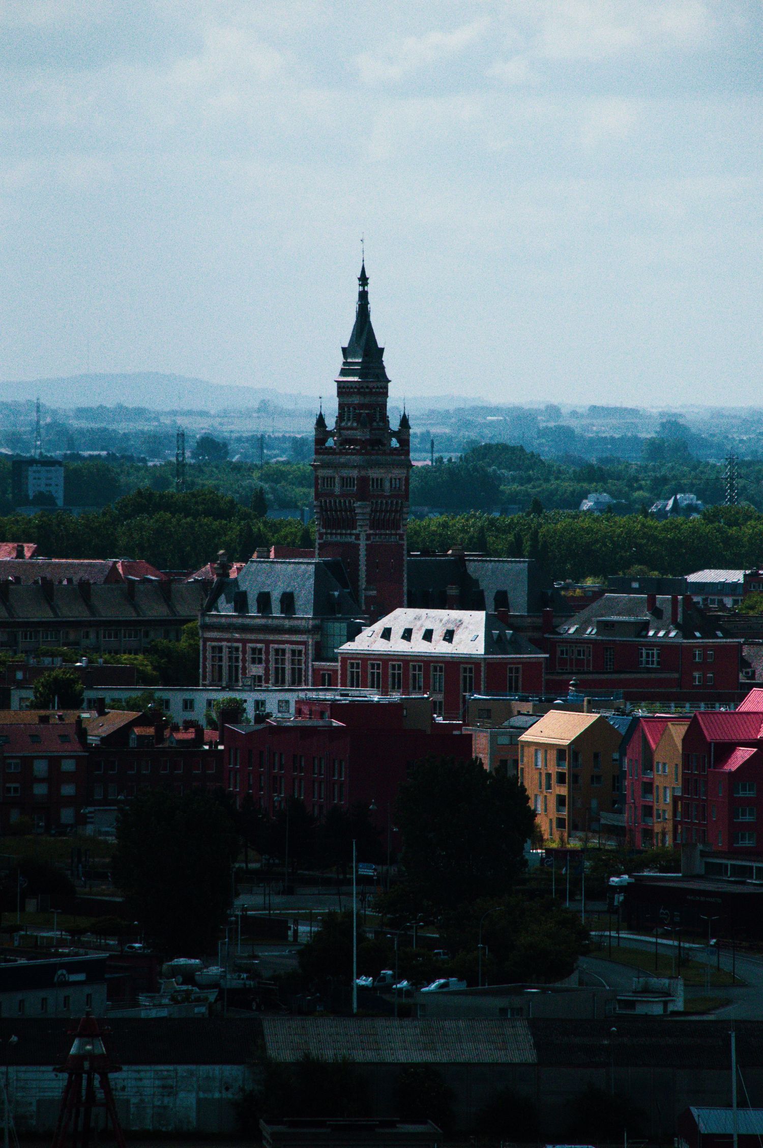 Aerial view of a European city skyline featuring a historic clock tower surrounded by colorful buildings and lush green trees.