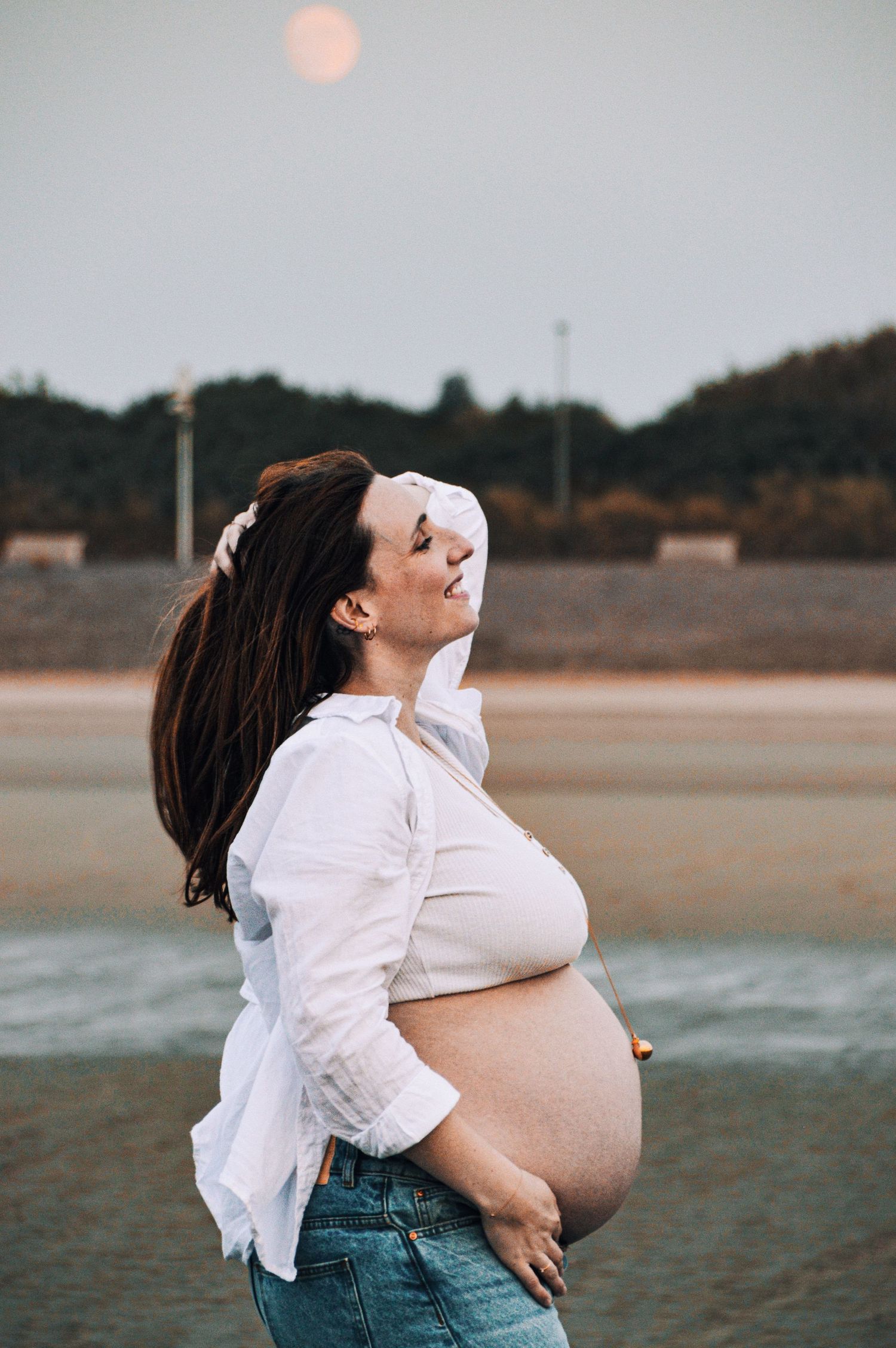 Sunset maternity photos on a beach with dramatic lighting and natural poses.