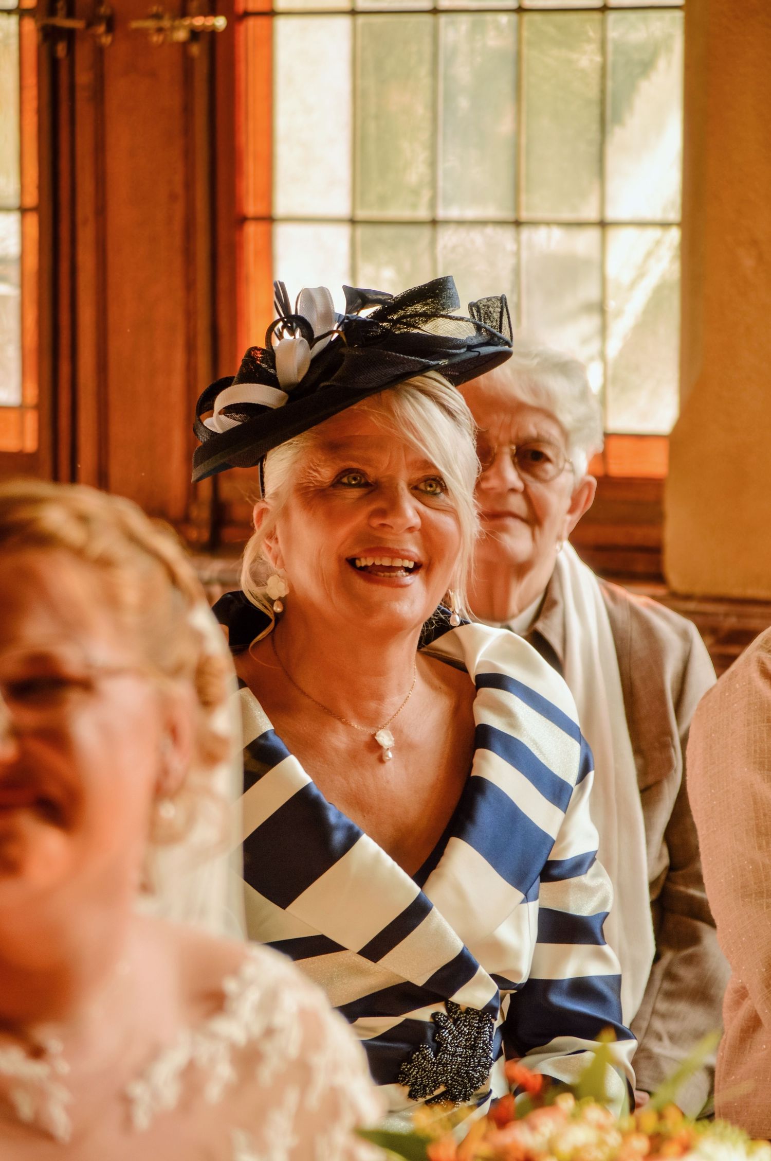 Wedding reception guests enjoying themselves in warm natural lighting through window panes.