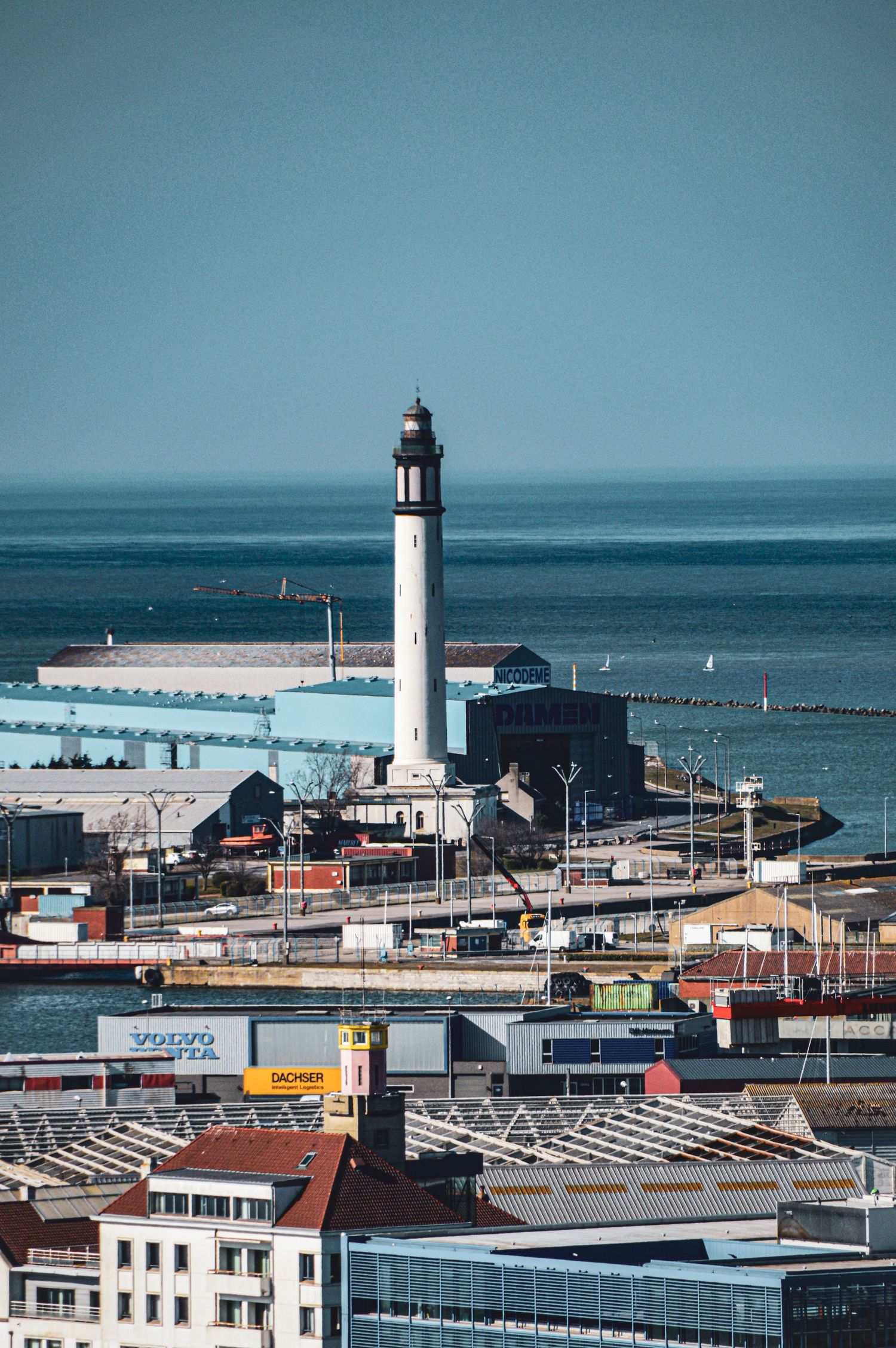 Maritime cityscape with lighthouse and harbor buildings along the coastline.