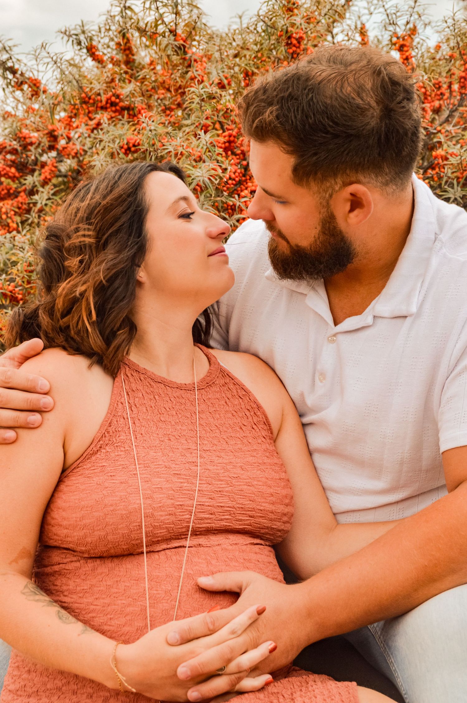 Intimate couple pose against backdrop of orange berries and sunlight.