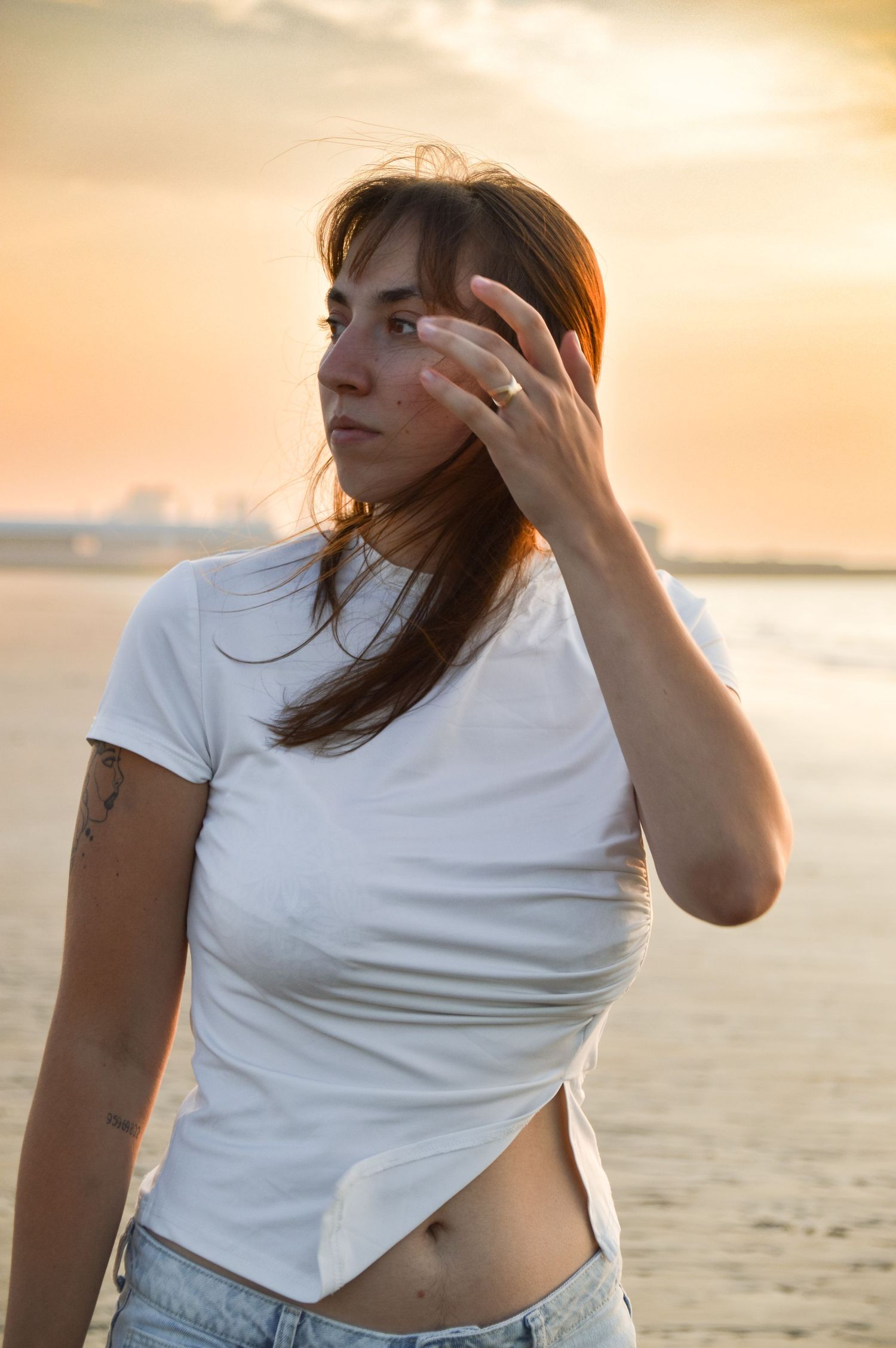 Woman in white shirt posing at beach during golden hour sunset.