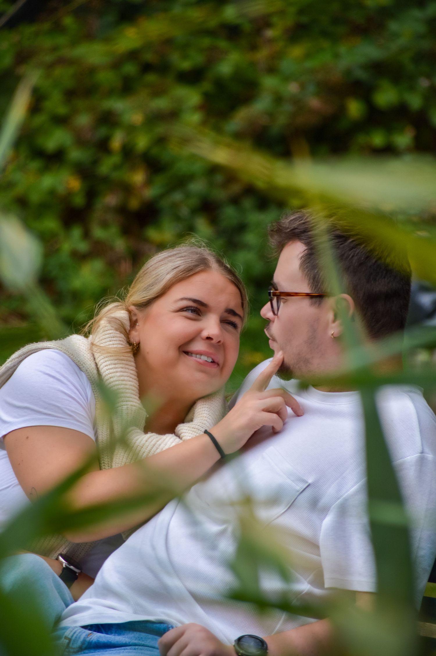 Couple sharing playful moment while relaxing outdoors among greenery.