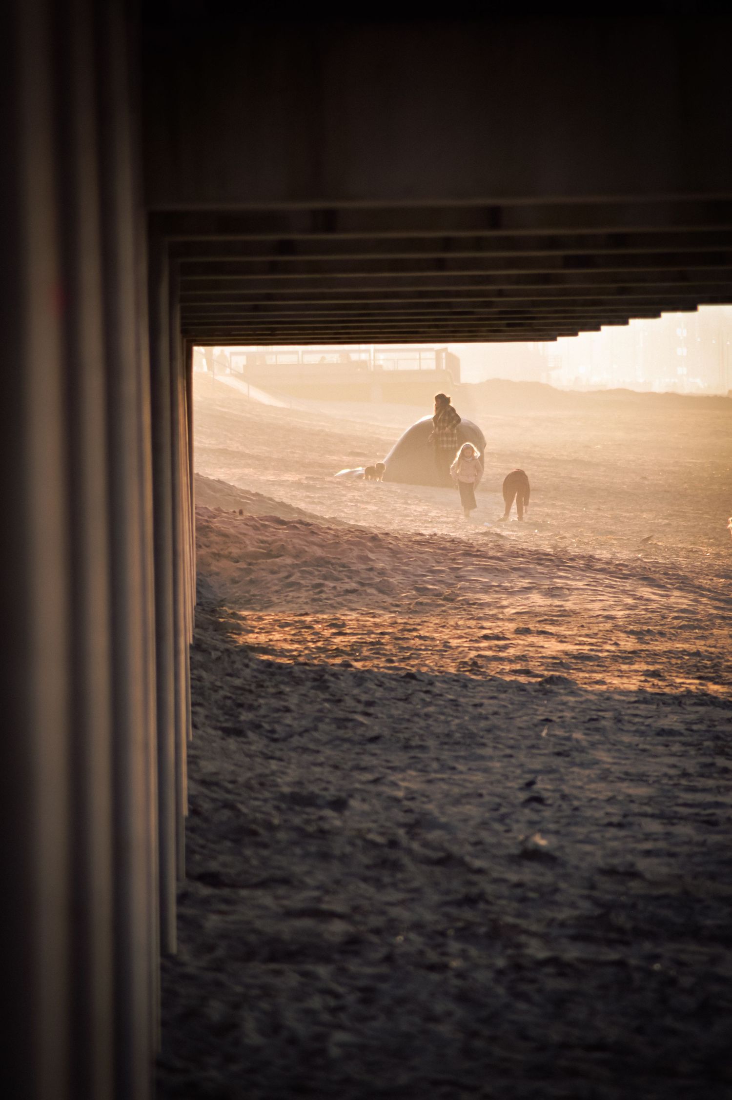 Silhouetted figures walking on beach at sunset viewed through architectural columns.