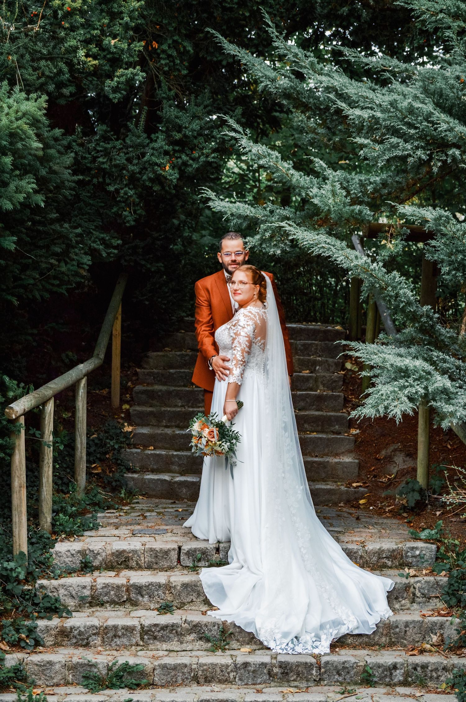 Wedding photos on stone steps surrounded by lush greenery and trees.