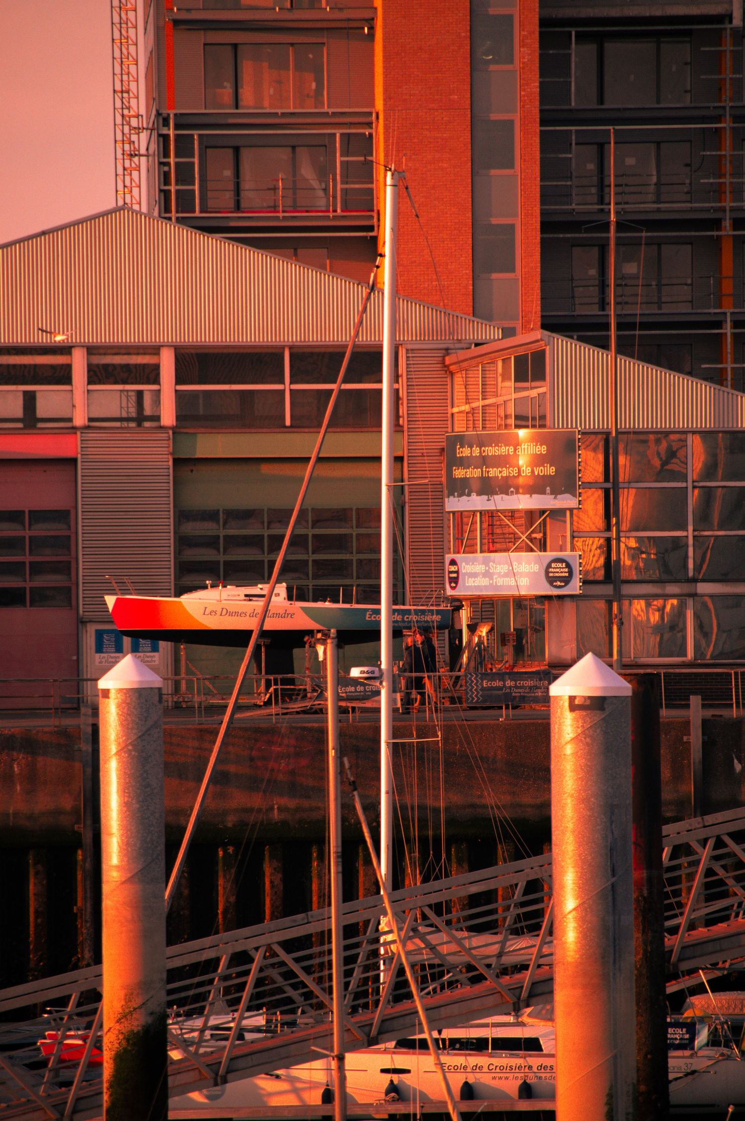 Sunset light illuminates waterfront buildings and wooden dock posts at a marina during golden hour.