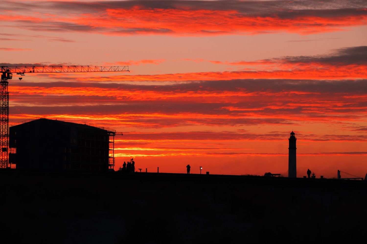 Urban skyline silhouetted against a fiery orange and red sunset sky.