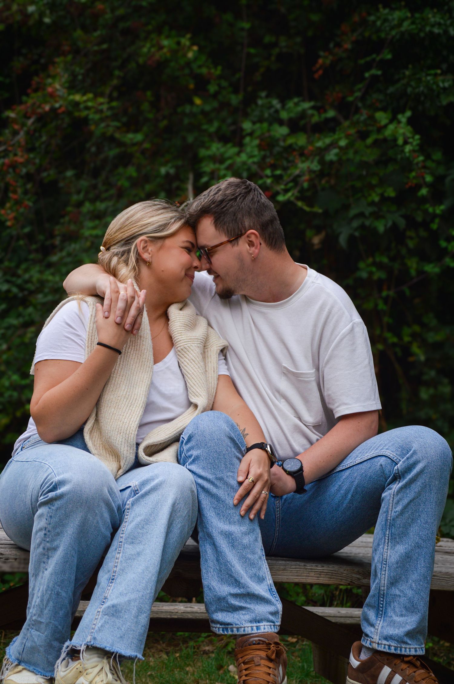 Couple sitting close together on wooden bench surrounded by greenery.