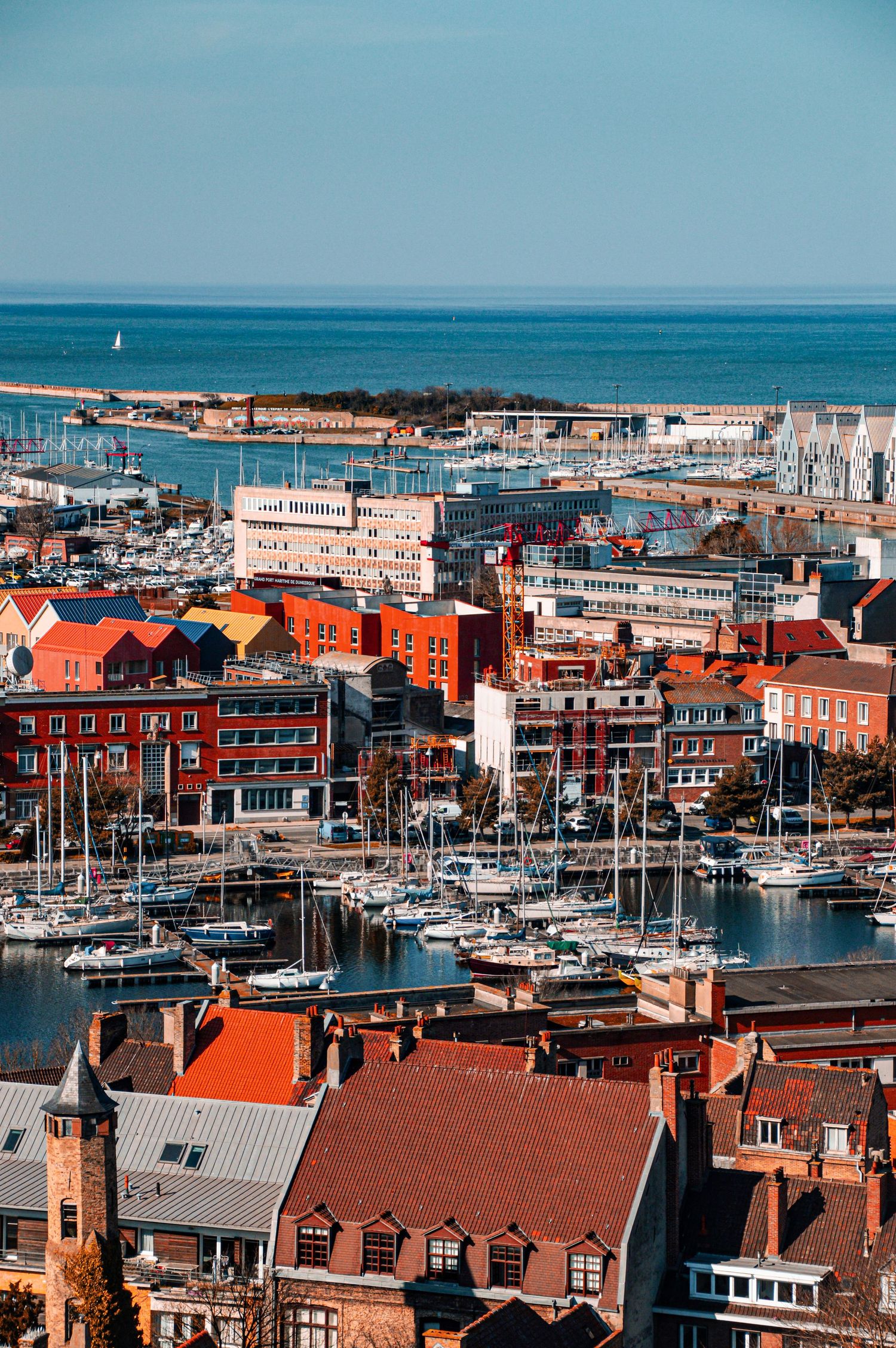 Aerial view of a coastal marina with orange-roofed buildings and boats docked in the harbor.