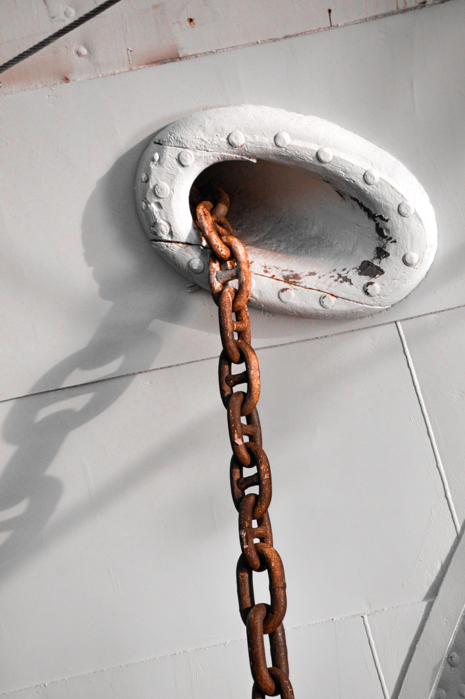 Rusty chain hanging from a white ceiling mount creating dramatic shadows.
