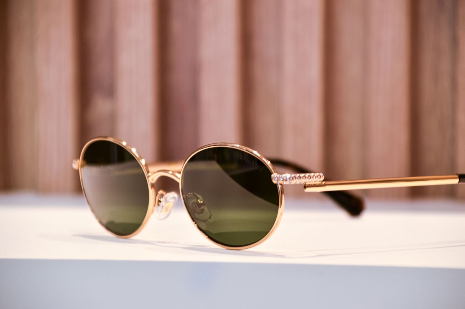 Round gold-framed sunglasses with dark green lenses photographed at an angle on white surface.