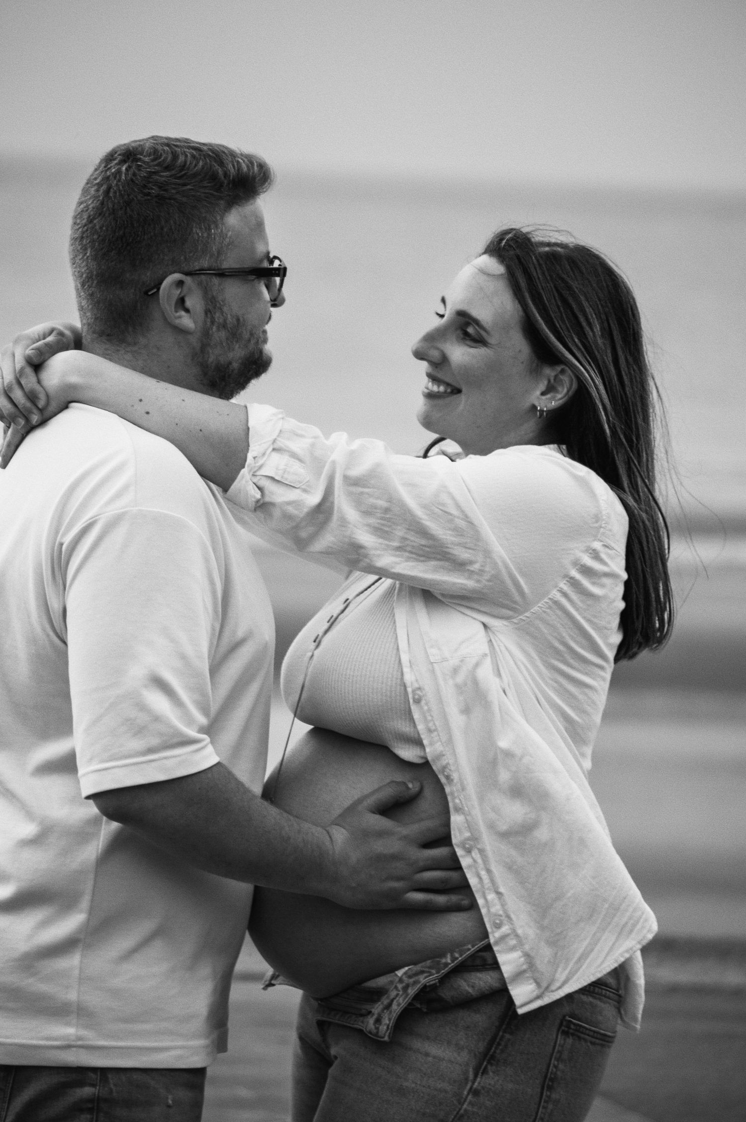 A couple in white shirts shares playful embraces during a beachside photoshoot.