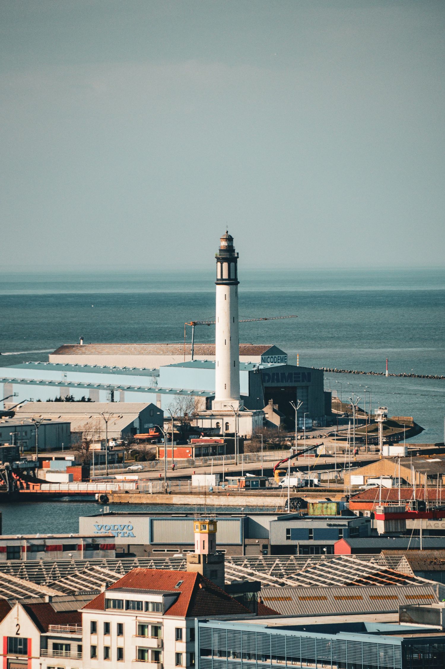 Coastal lighthouse and harbor buildings against a misty ocean backdrop.