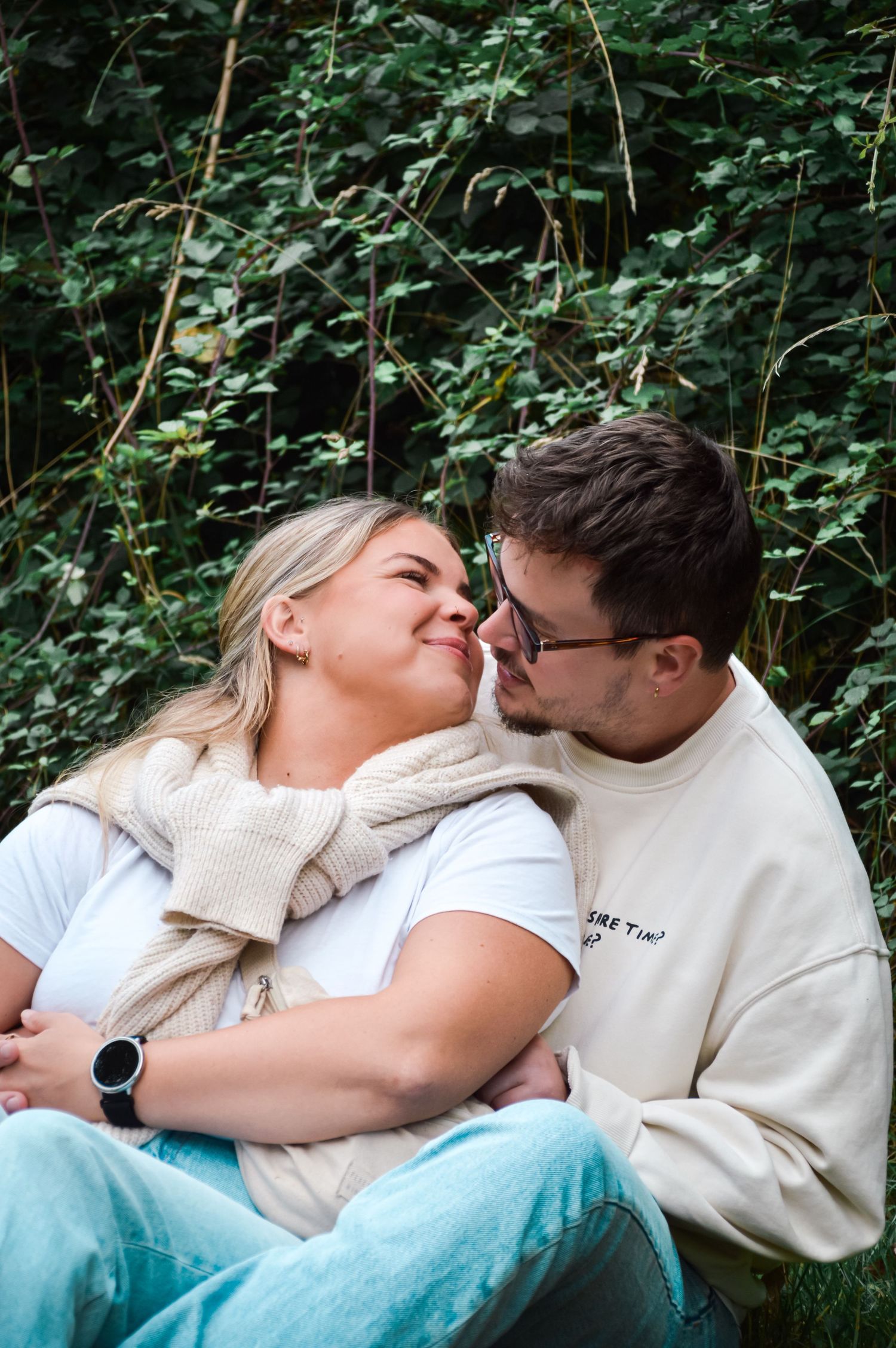 A couple sharing an intimate moment while resting on grass in a garden setting.