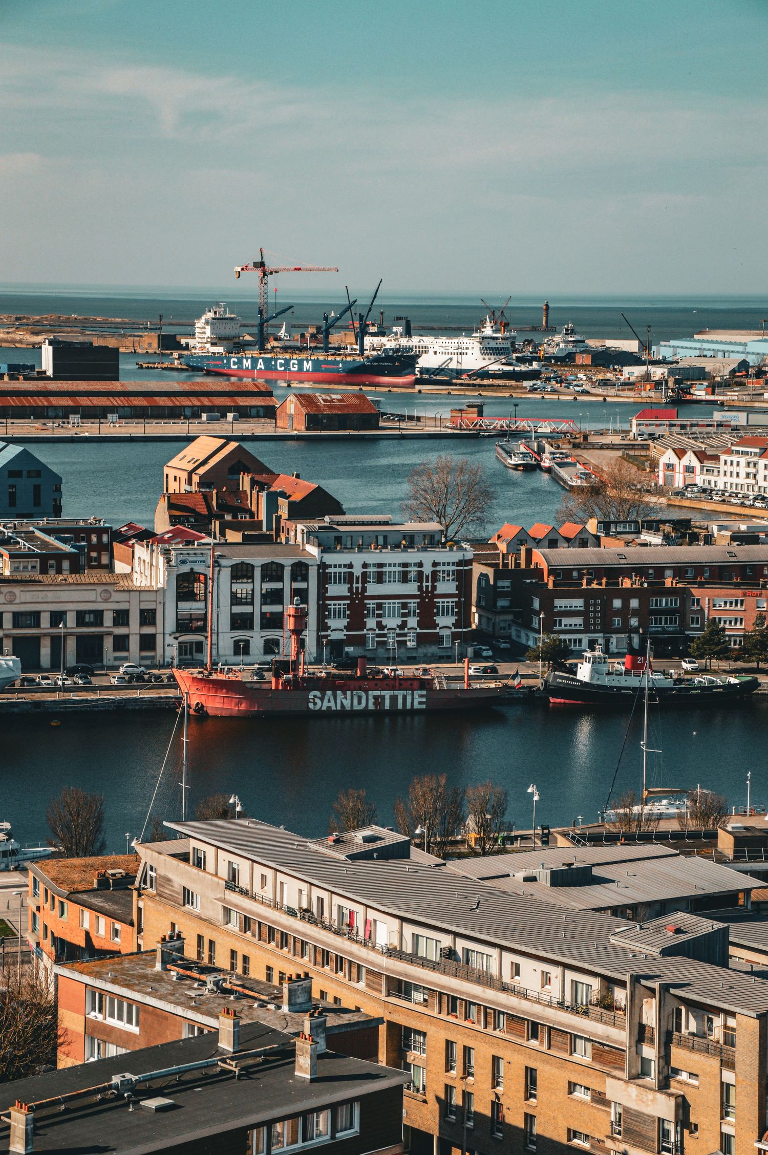 Panoramic harbor view with industrial buildings, ships, and waterfront architecture.