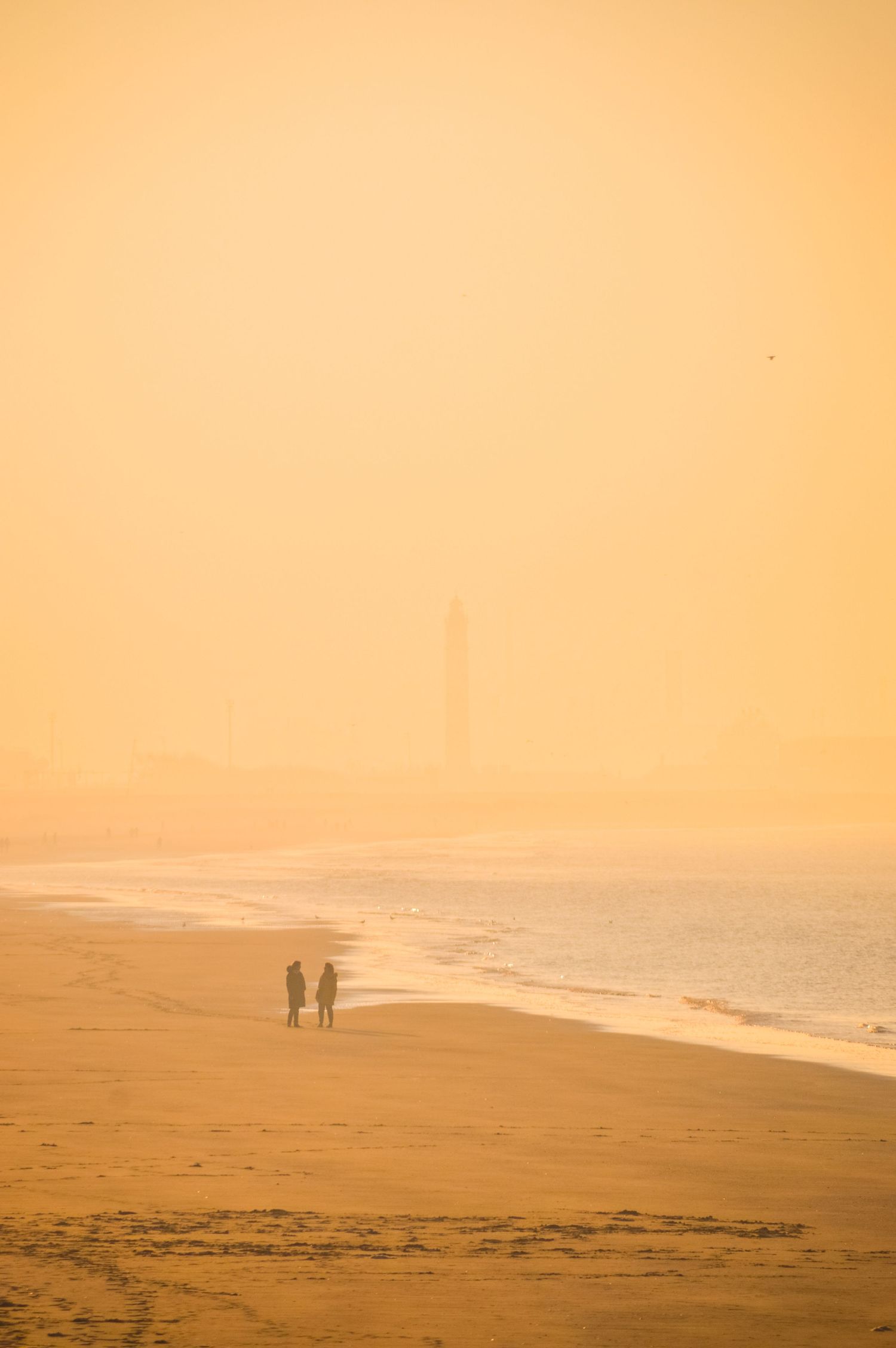 Distant figures walking on a misty beach at sunset with warm orange tones.