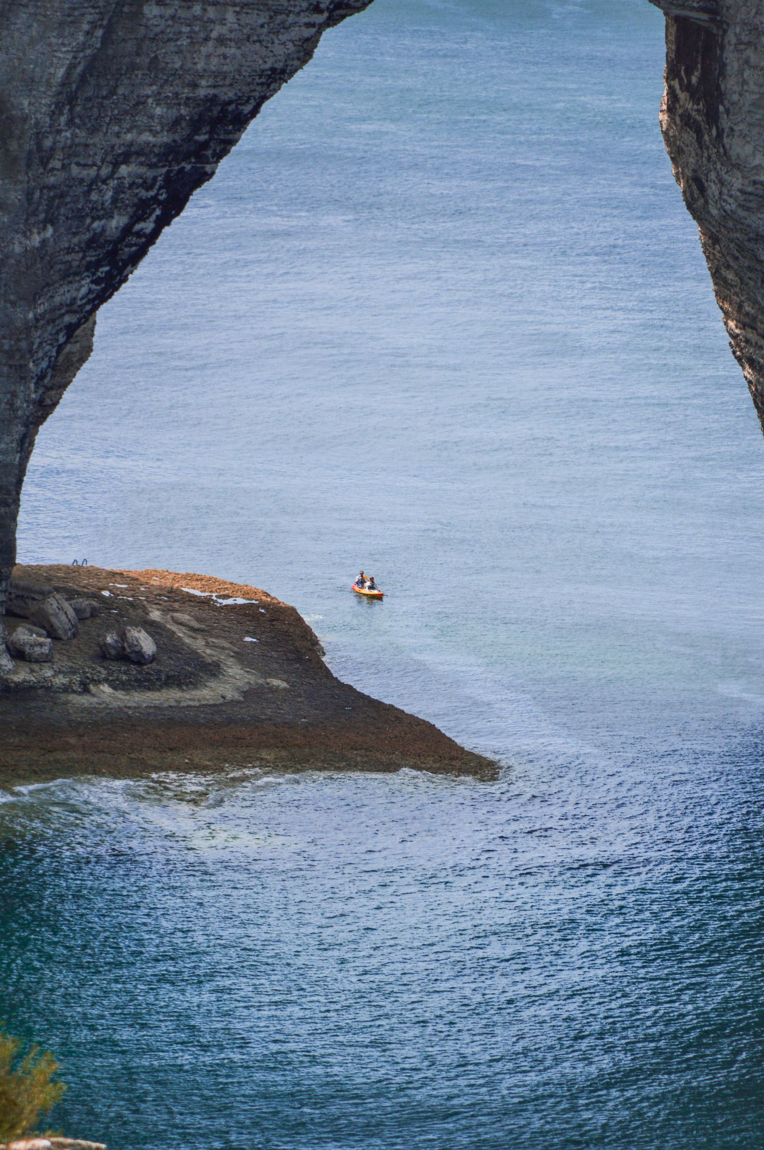 Small kayak visible through dramatic rocky coastal arch formation.