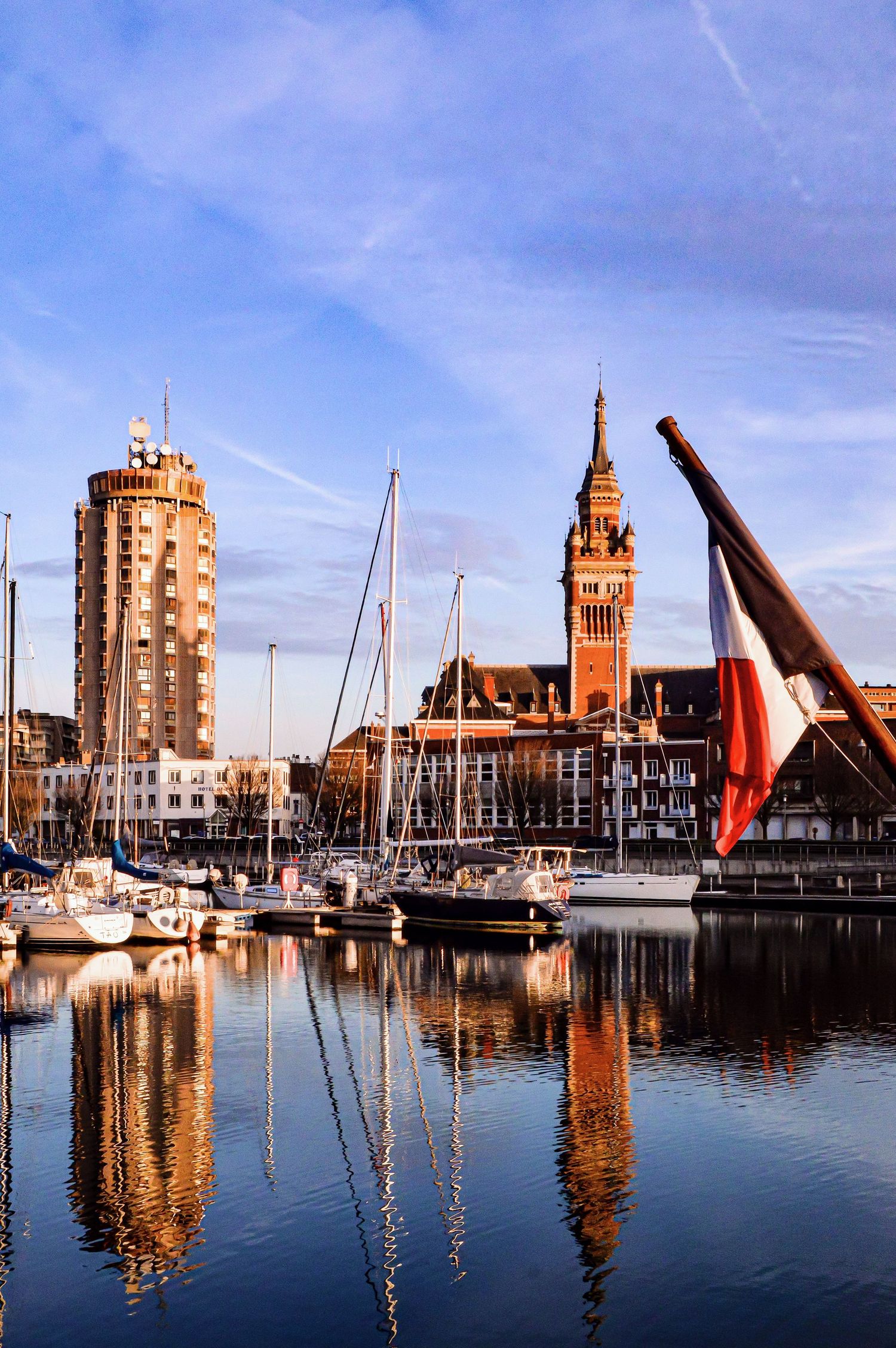 Panoramic view of marina with boats and distinctive tower architecture against blue sky.