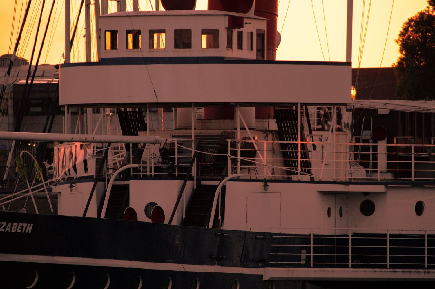 A vintage steamship named Elizabeth docked at harbor during a golden sunset, with warm light reflecting off its white and black hull.