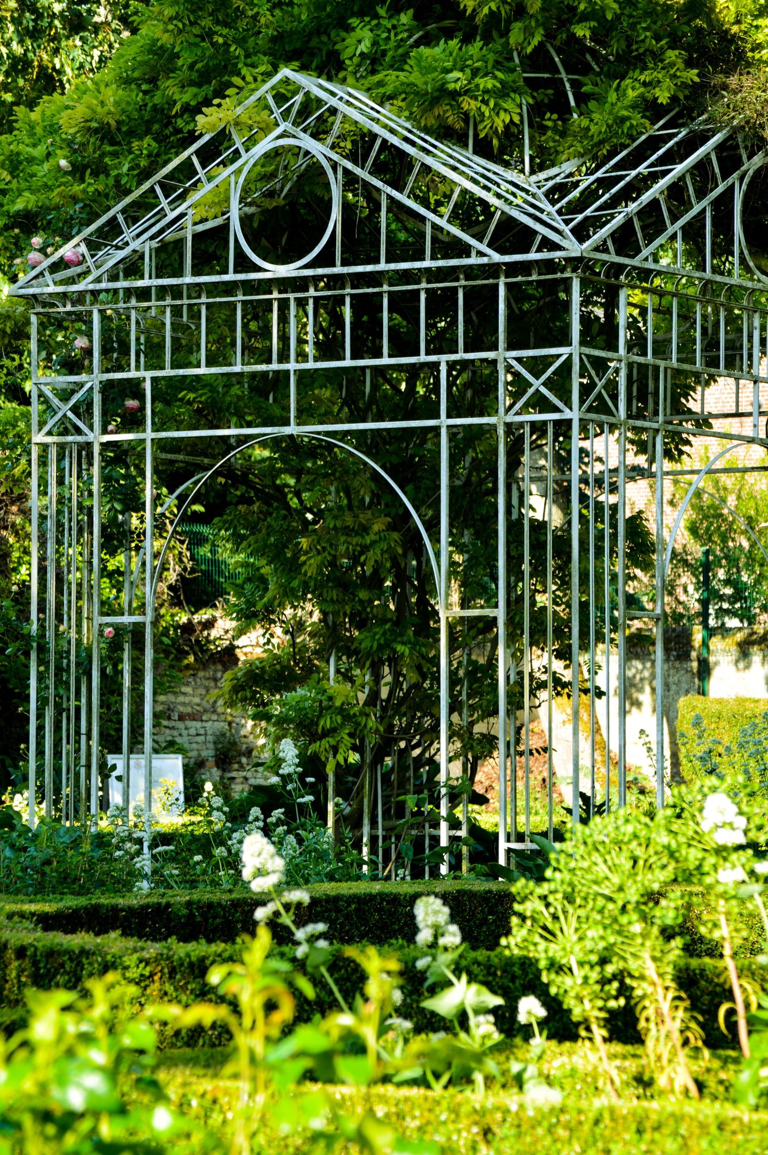 Decorative metal garden arbor structures create an elegant pathway through lush green landscaping.