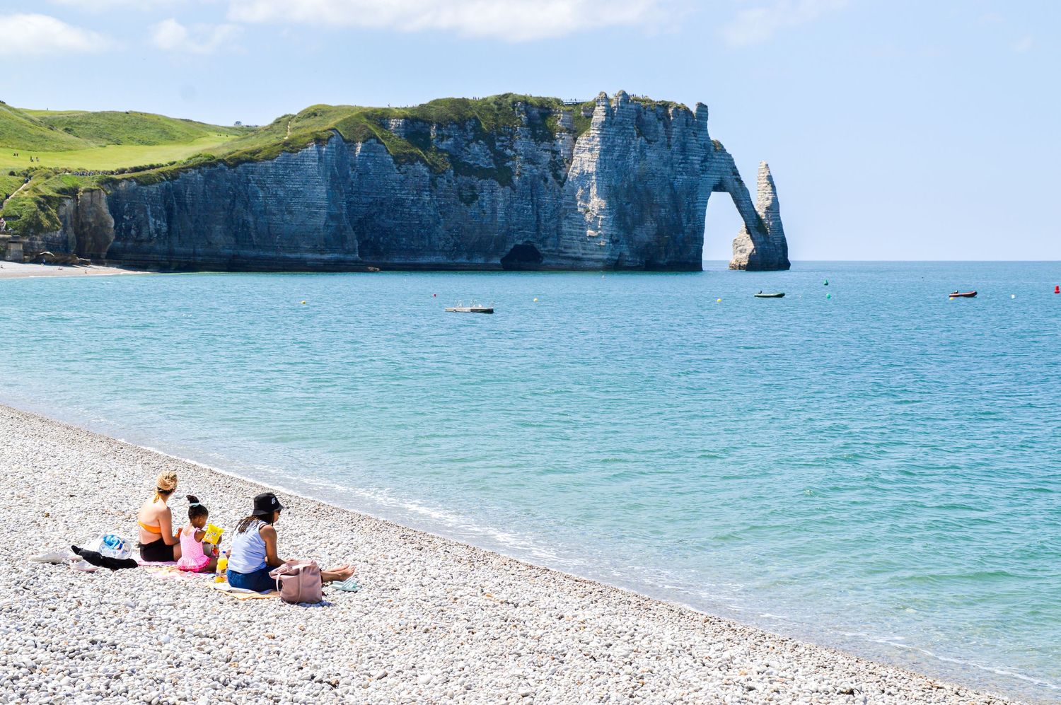 Beachgoers enjoy the pebble shoreline with views of Etretat's famous natural arch formation.