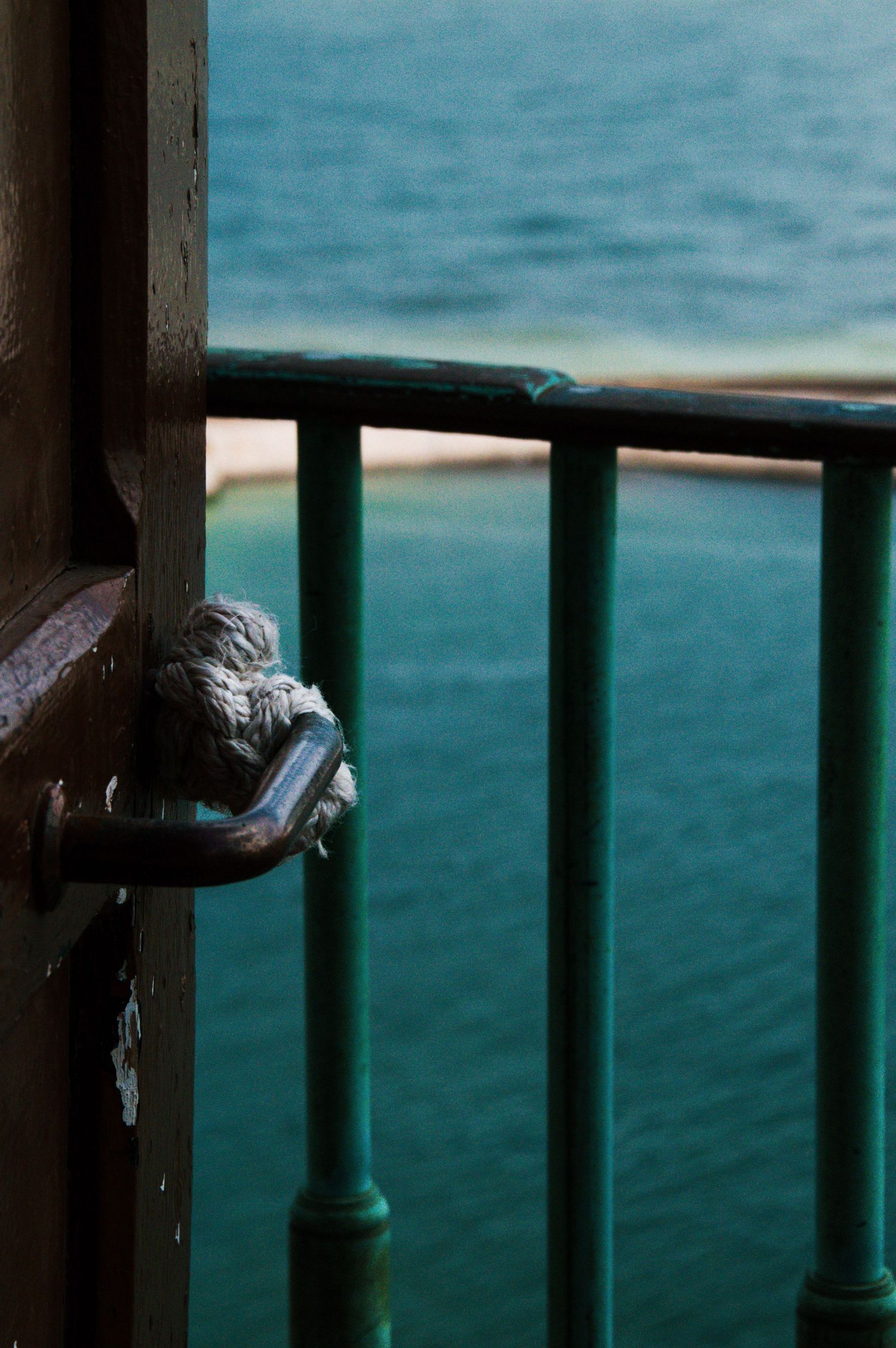 Rusty metal door handle on a weathered railing overlooking turquoise ocean water, vintage maritime architecture detail.