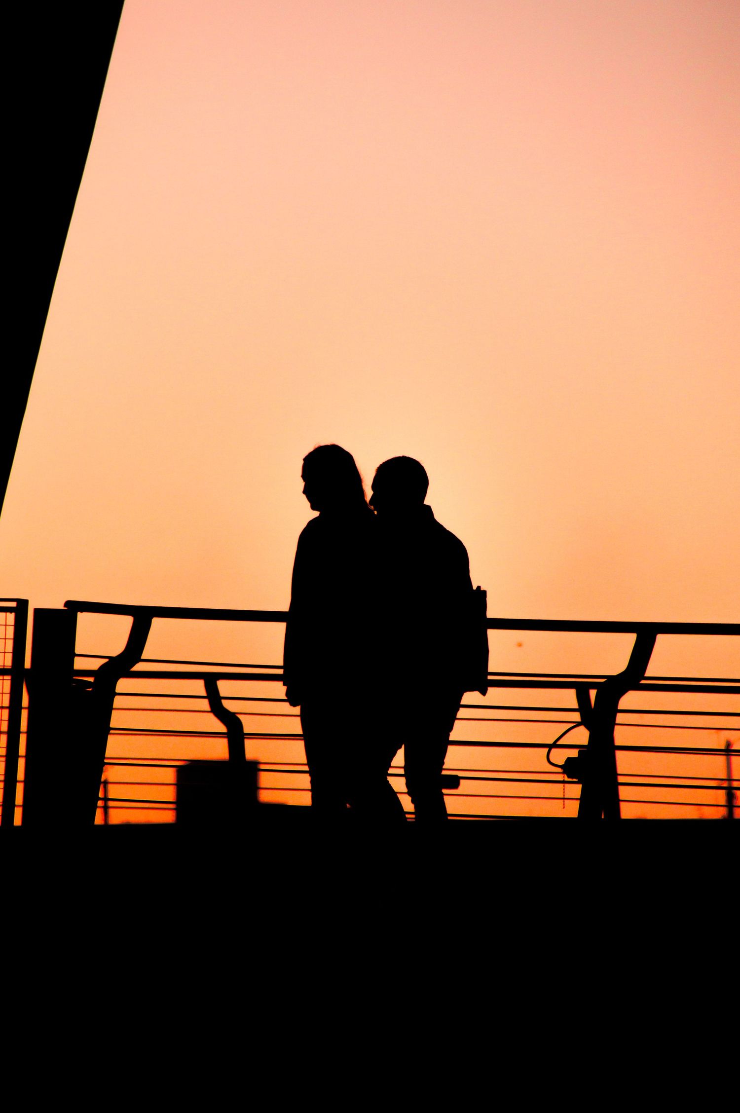 Silhouettes of people standing on a pier against a vibrant orange sunset sky.