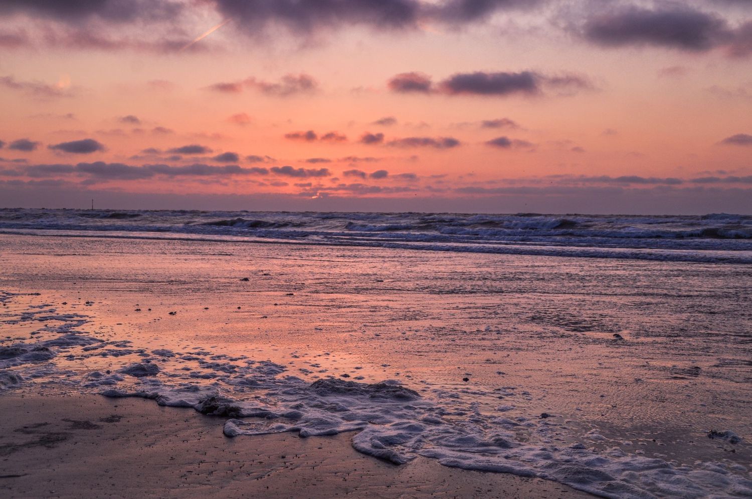 Pink and purple sunset sky reflects on wet beach sand during low tide.