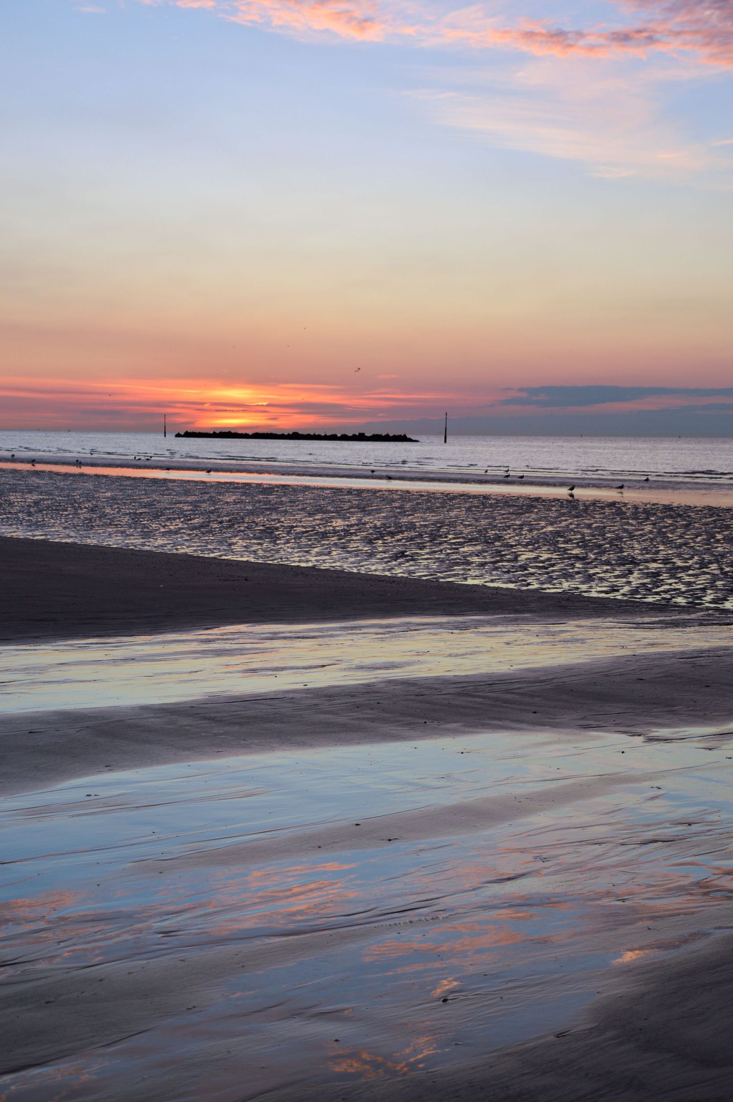 Stunning beach sunset with pink and orange sky reflecting on wet sand.