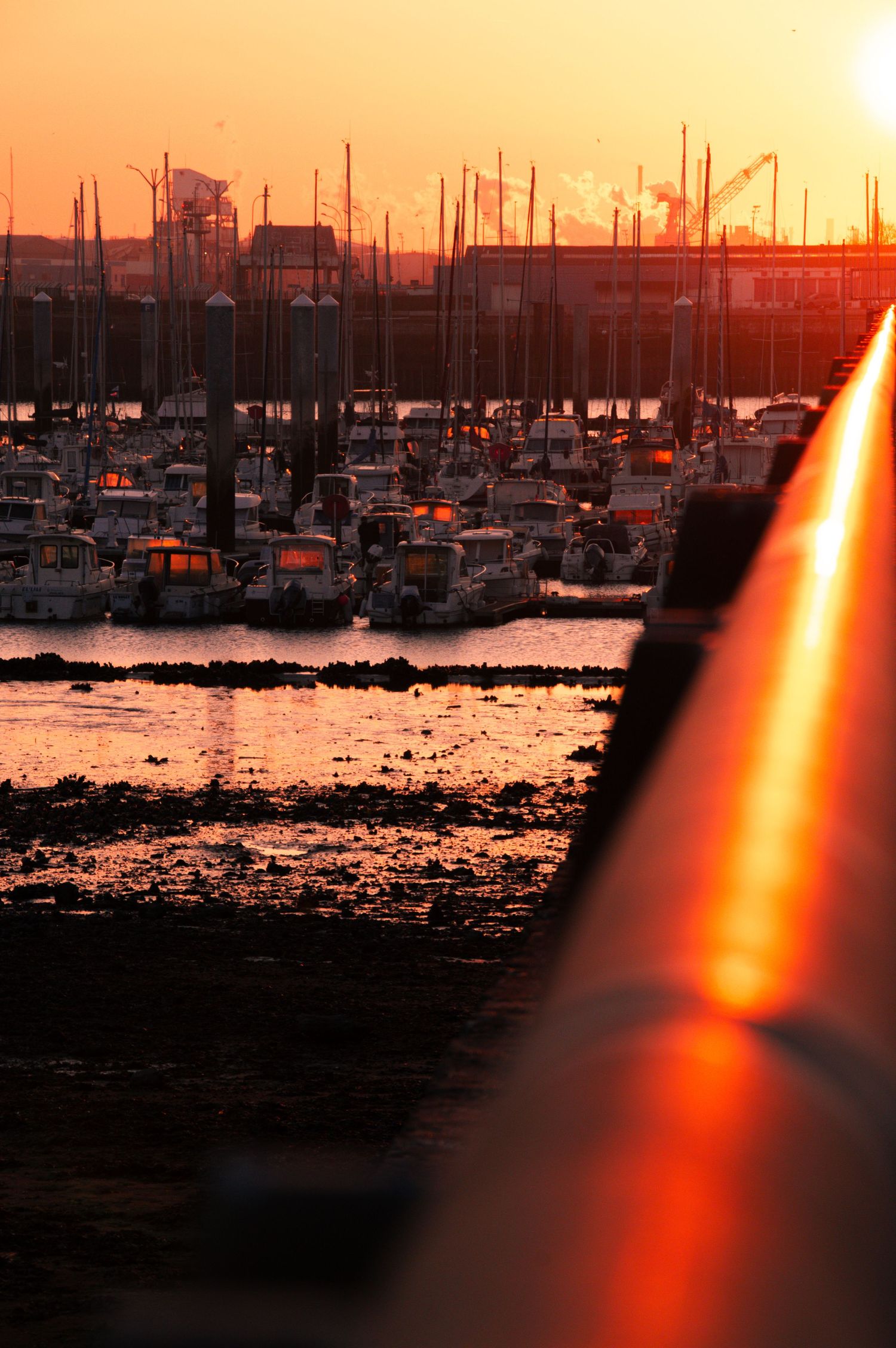 Dramatic orange sunset silhouettes boats in a marina harbor with light beams reflecting across dark waters.