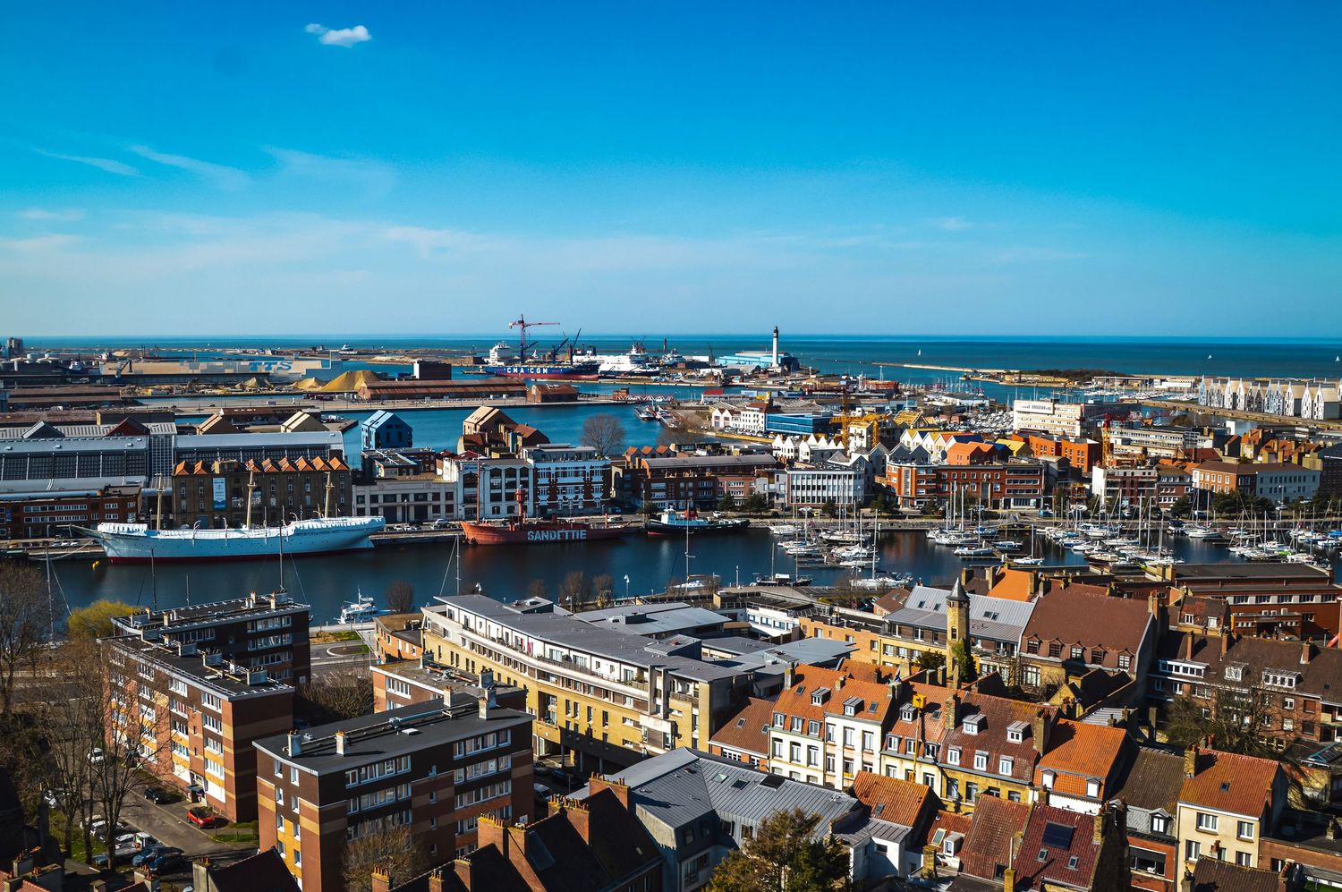 Panoramic aerial view of a coastal city harbor with buildings and industrial structures.