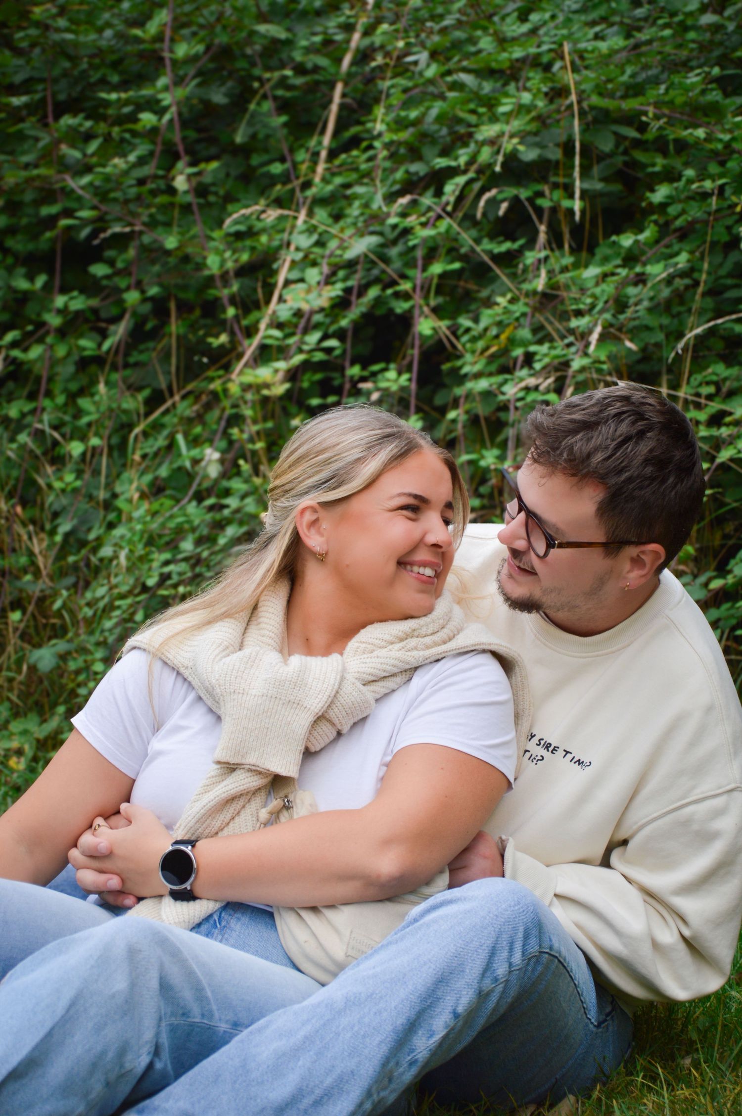 Two people relaxing together on grass surrounded by lush greenery.